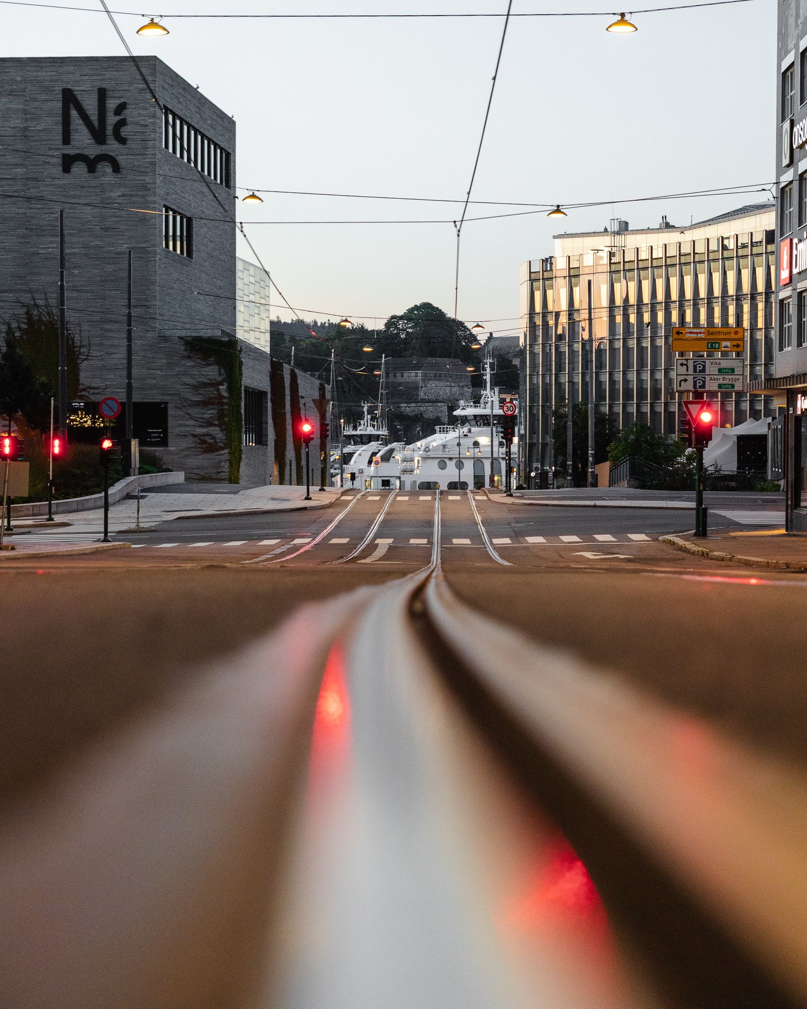 Tømmerkaj i Tønsberg med trikkelinjer, røde trafikklys og historiske bygninger ved solnedgang.