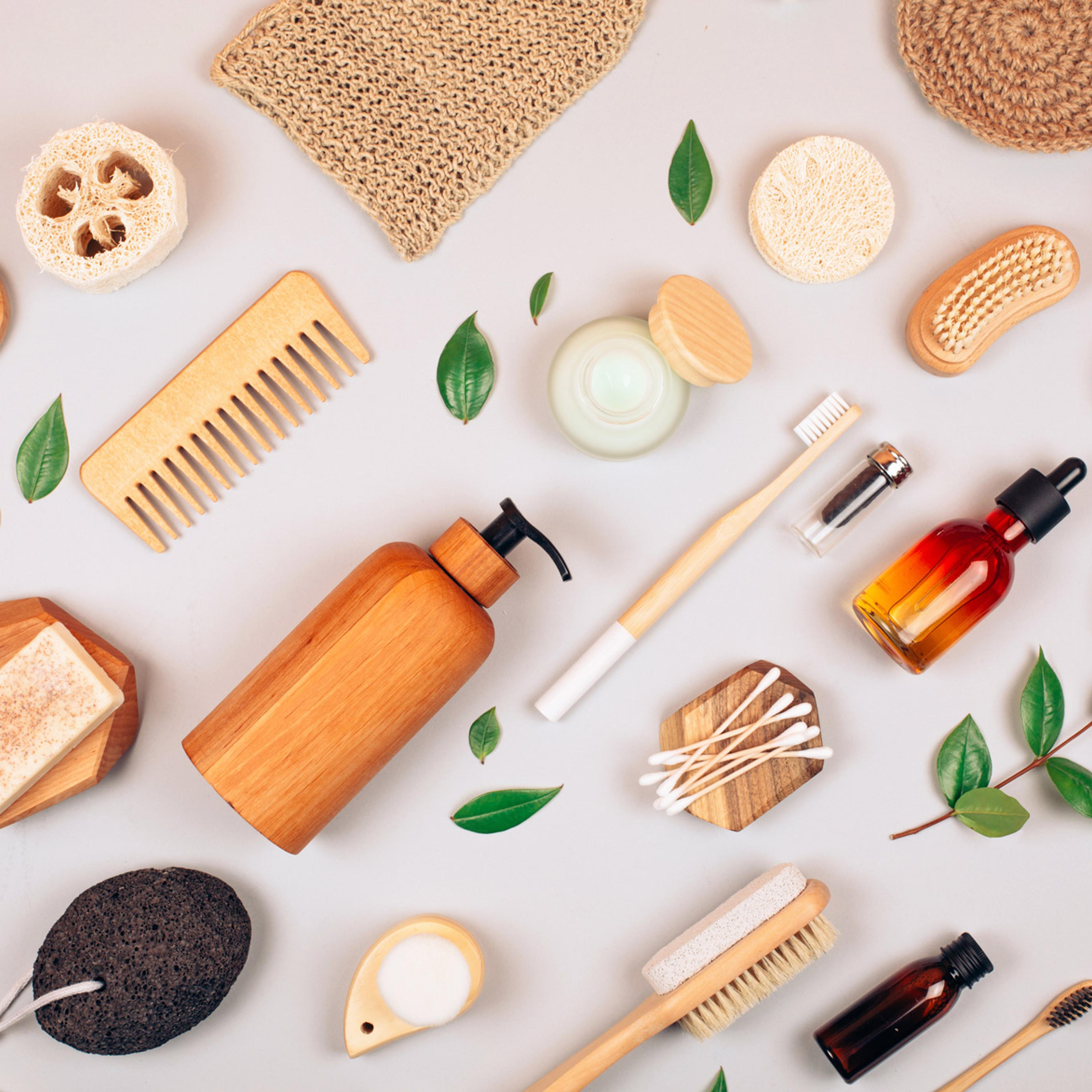 Flat lay av naturlige skjøtselsprodukter med børster, svamper, kremer og essensielle oljer på grå bakgrunn.