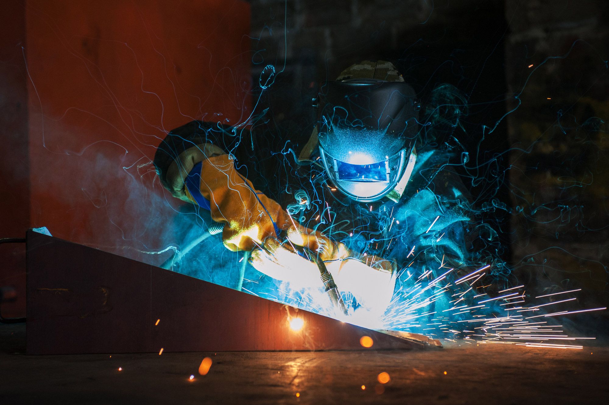 Elektrodesveisingarbeid med intens lysbue og gnister fra sveisetang på metalloverflate