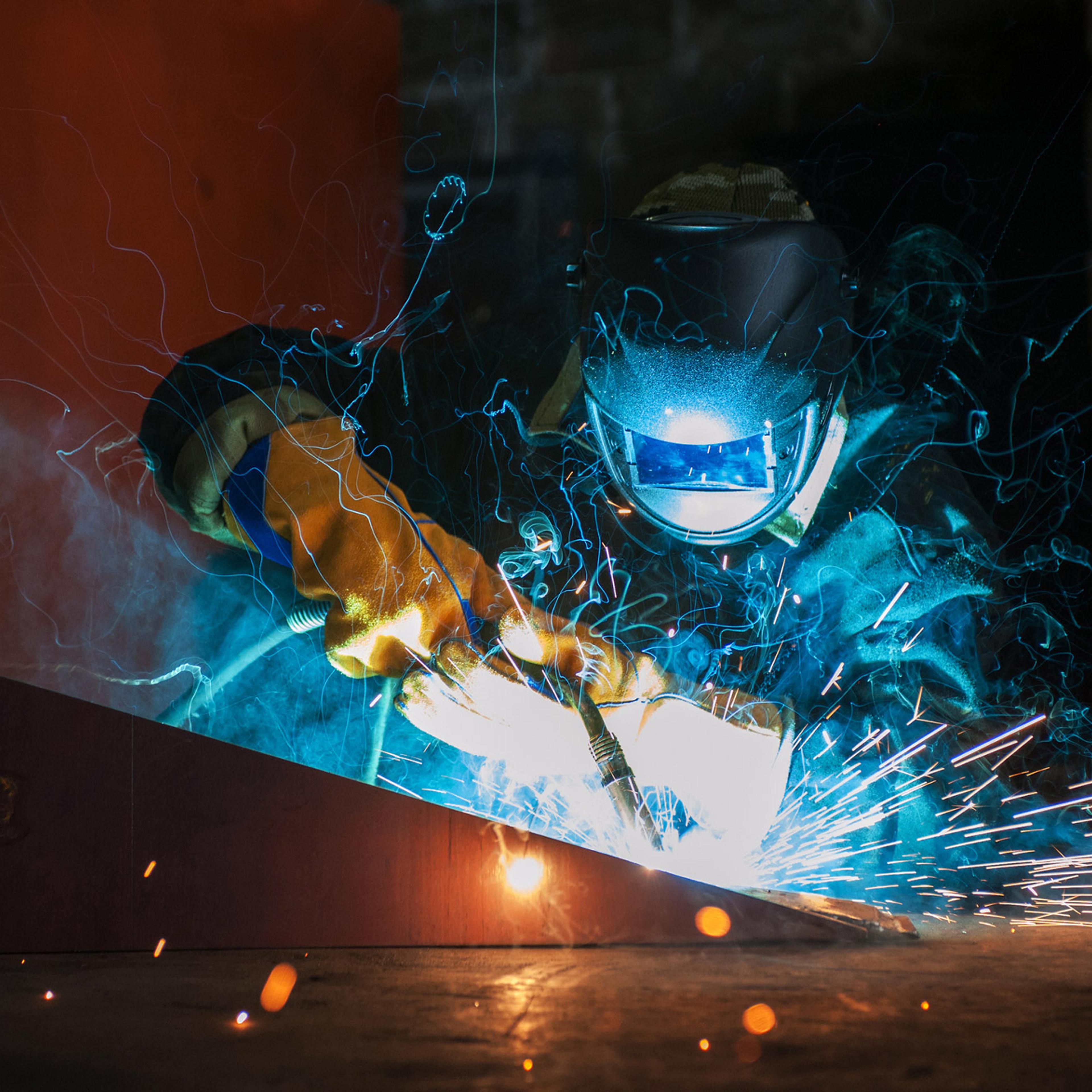 Elektrodesveisingarbeid med intens lysbue og gnister fra sveisetang på metalloverflate