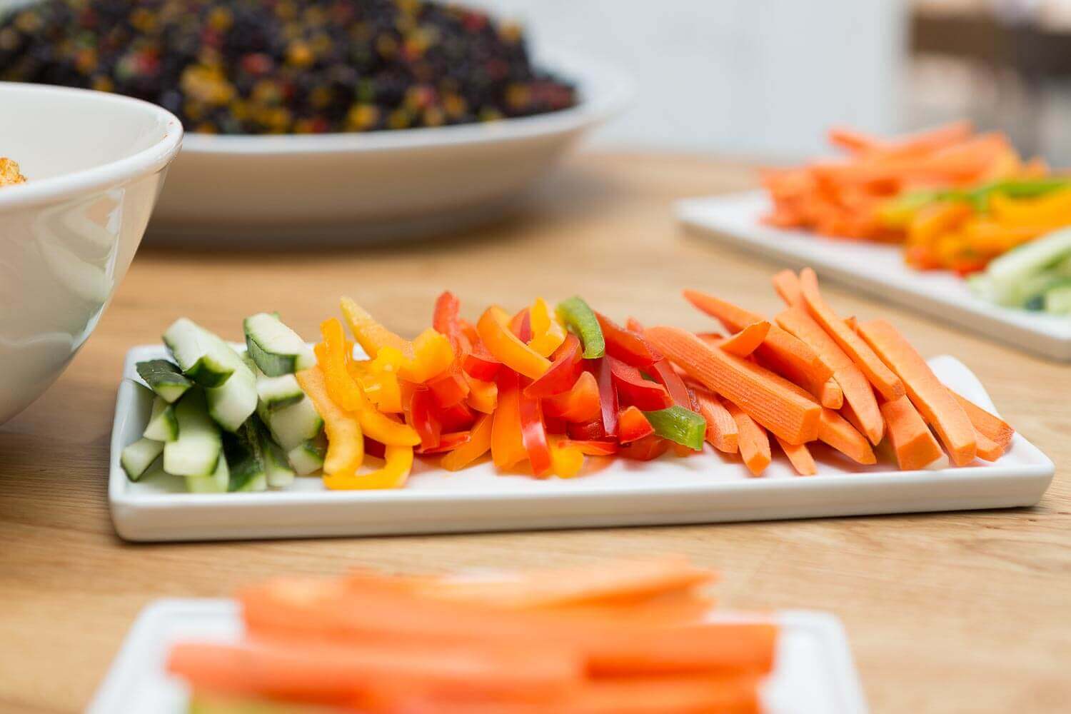 Fargefulle grønnsaksstrimler arrangert på hvit tallerken – agurk, gul paprika, rød paprika og gulrot.