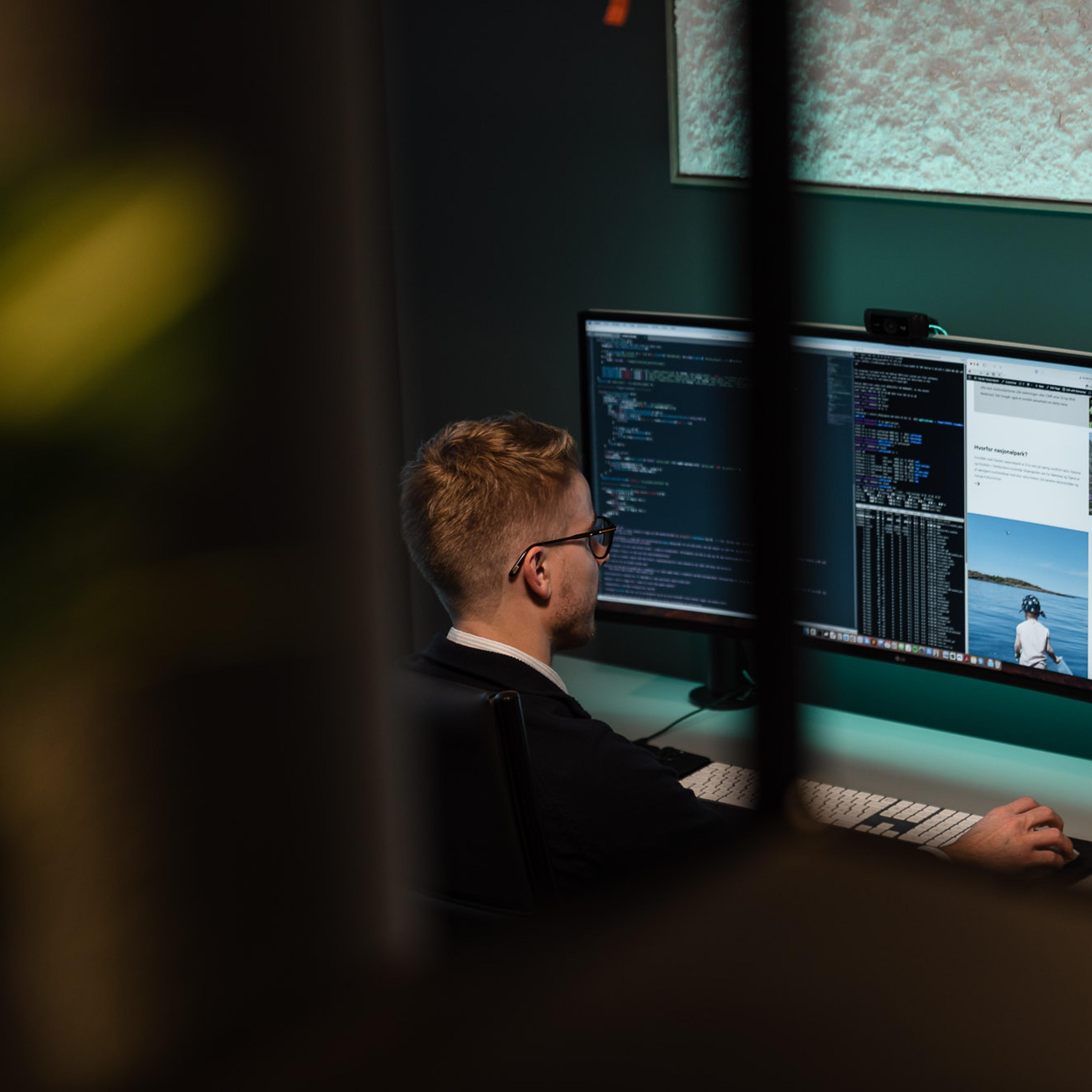 Mann ved skjerm arbeider med webdesign og koding i digitalt arbeidsmiljø.