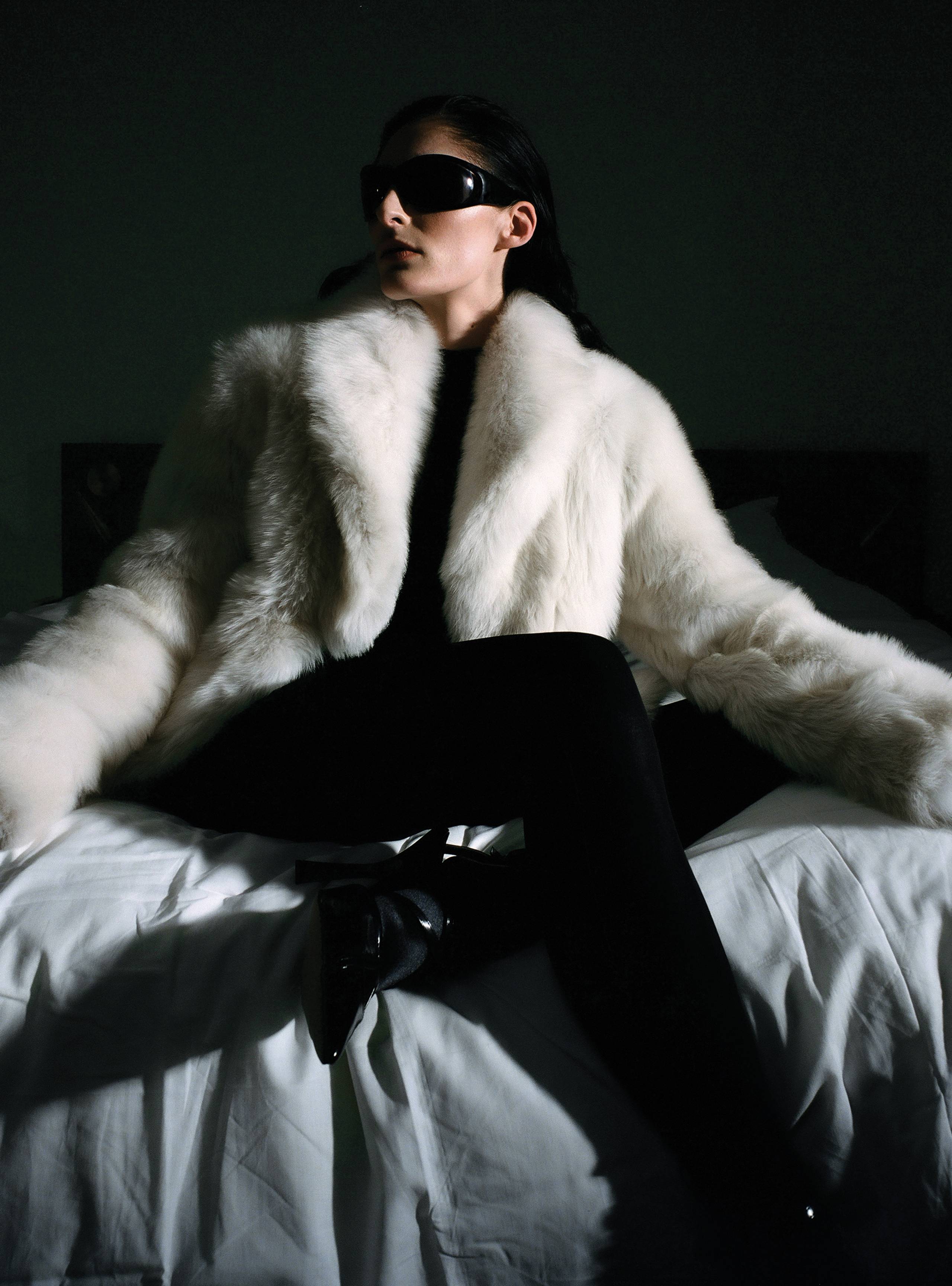 A model sitting on a bed wearing the Soiree cloud fluffy shearling coat