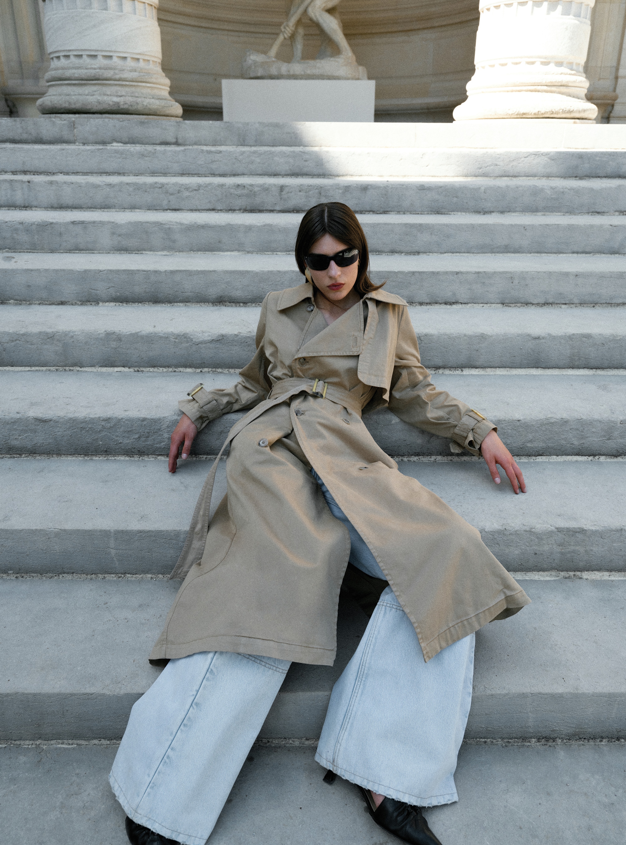 A model sitting on stairs wearing the Harriet Canvas Khaki trench