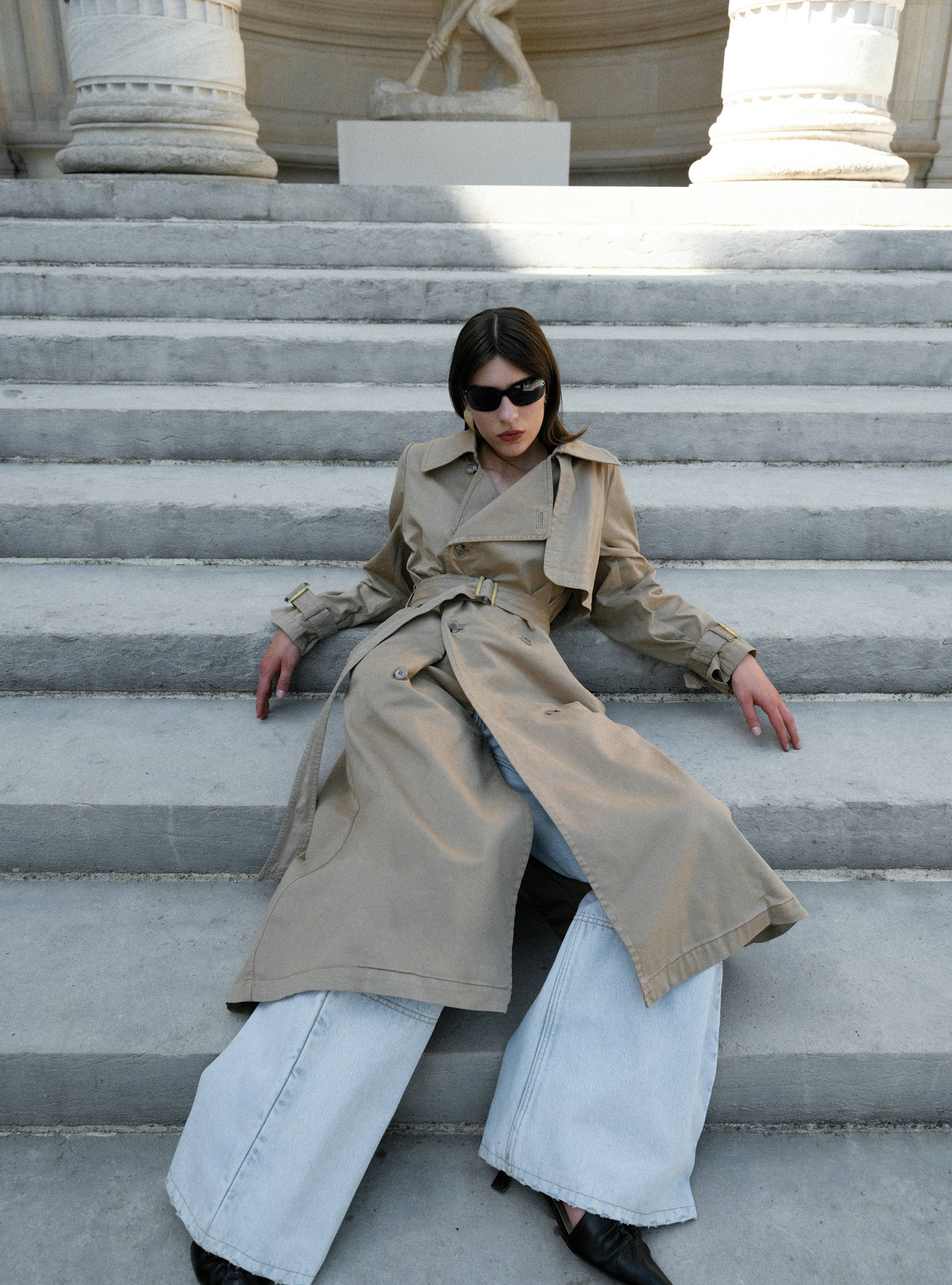 A model sitting on stairs wearing the Harriet Canvas Khaki trench