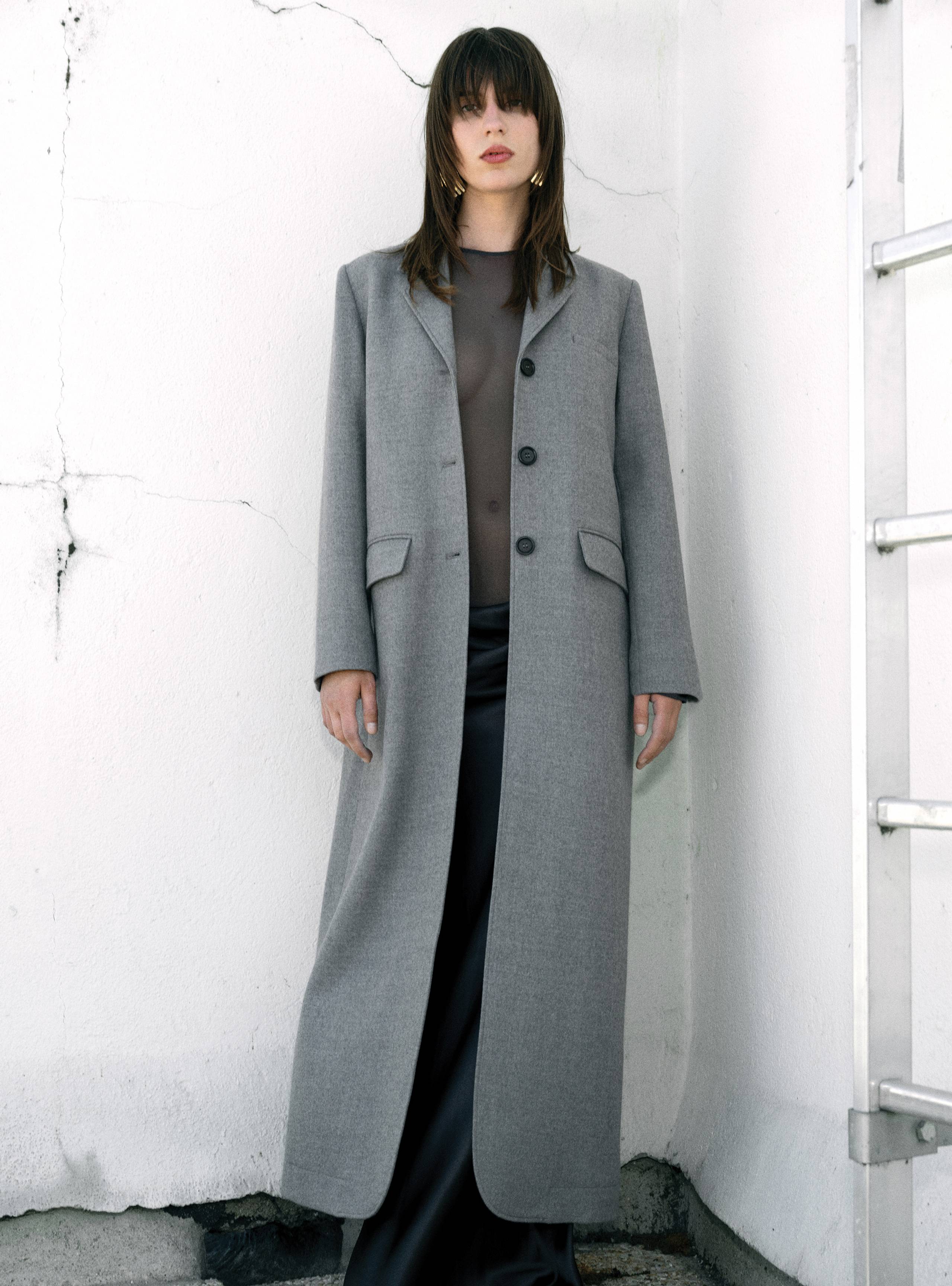 A model standing straight wearing the Celine Light Grey long suit coat