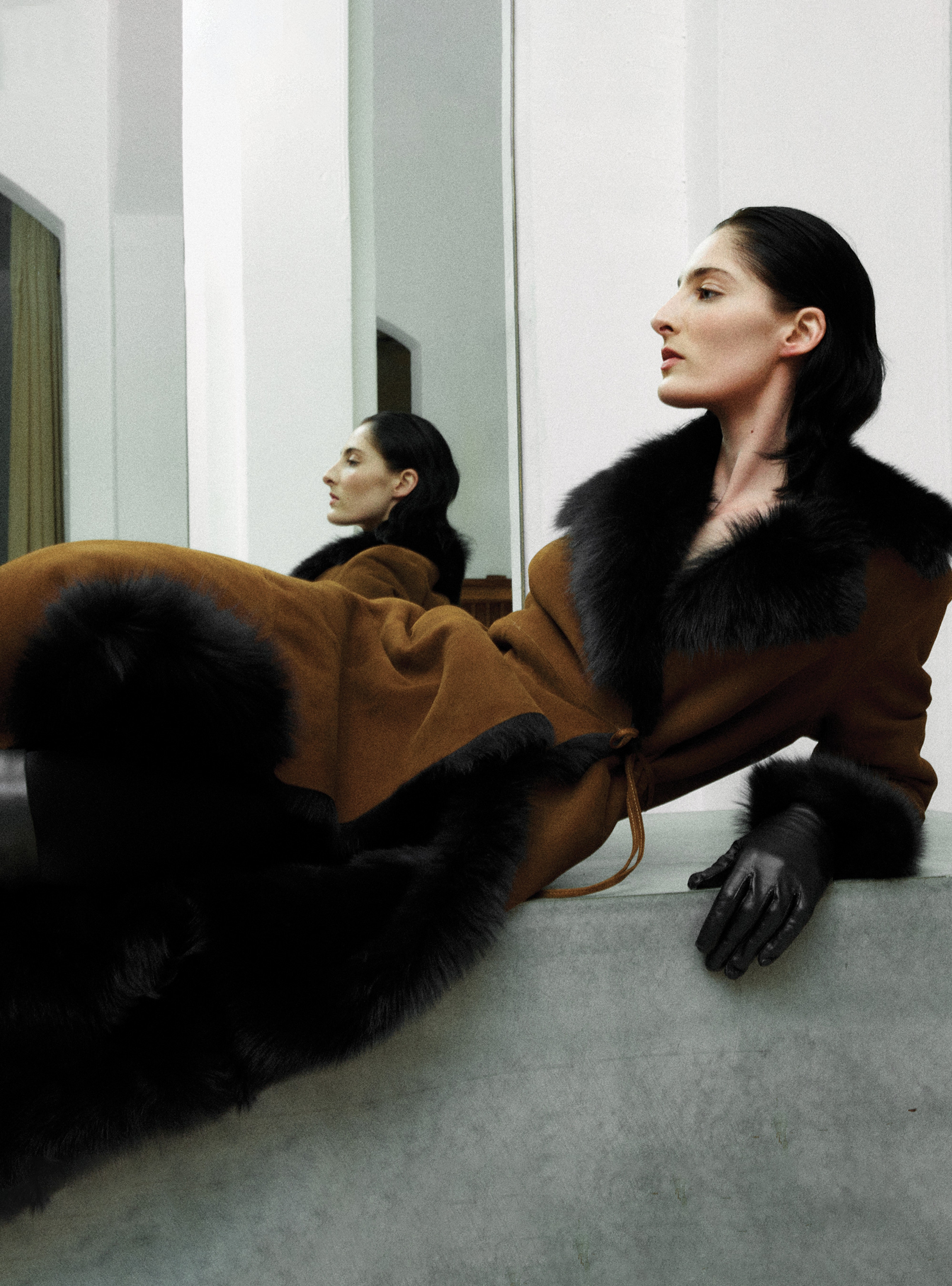 A model lying sideways wearing the Joni Cognac Black long shearling coat