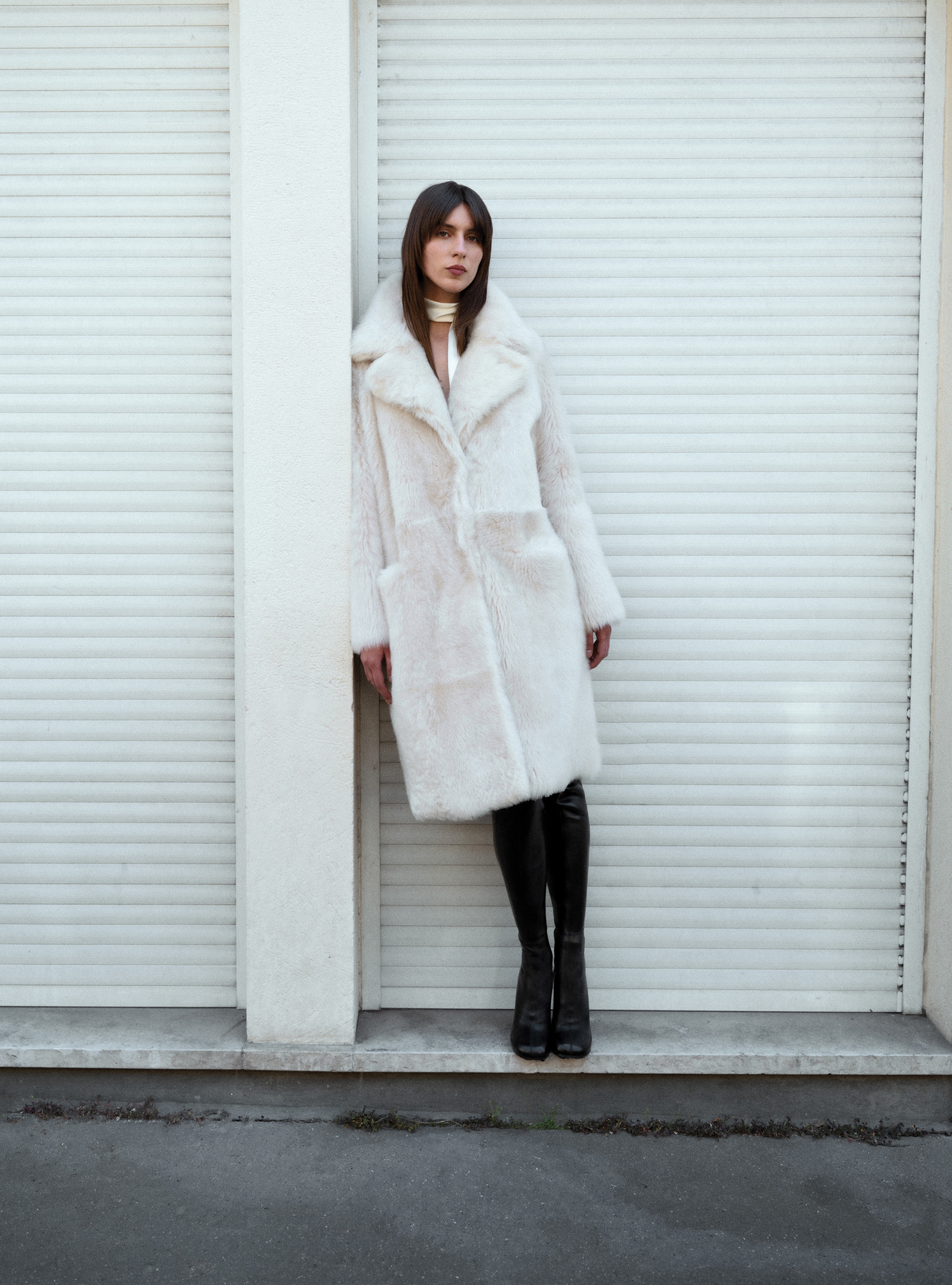 A model leaning sideways in the Evita Ivory Apres Ski shearling coat