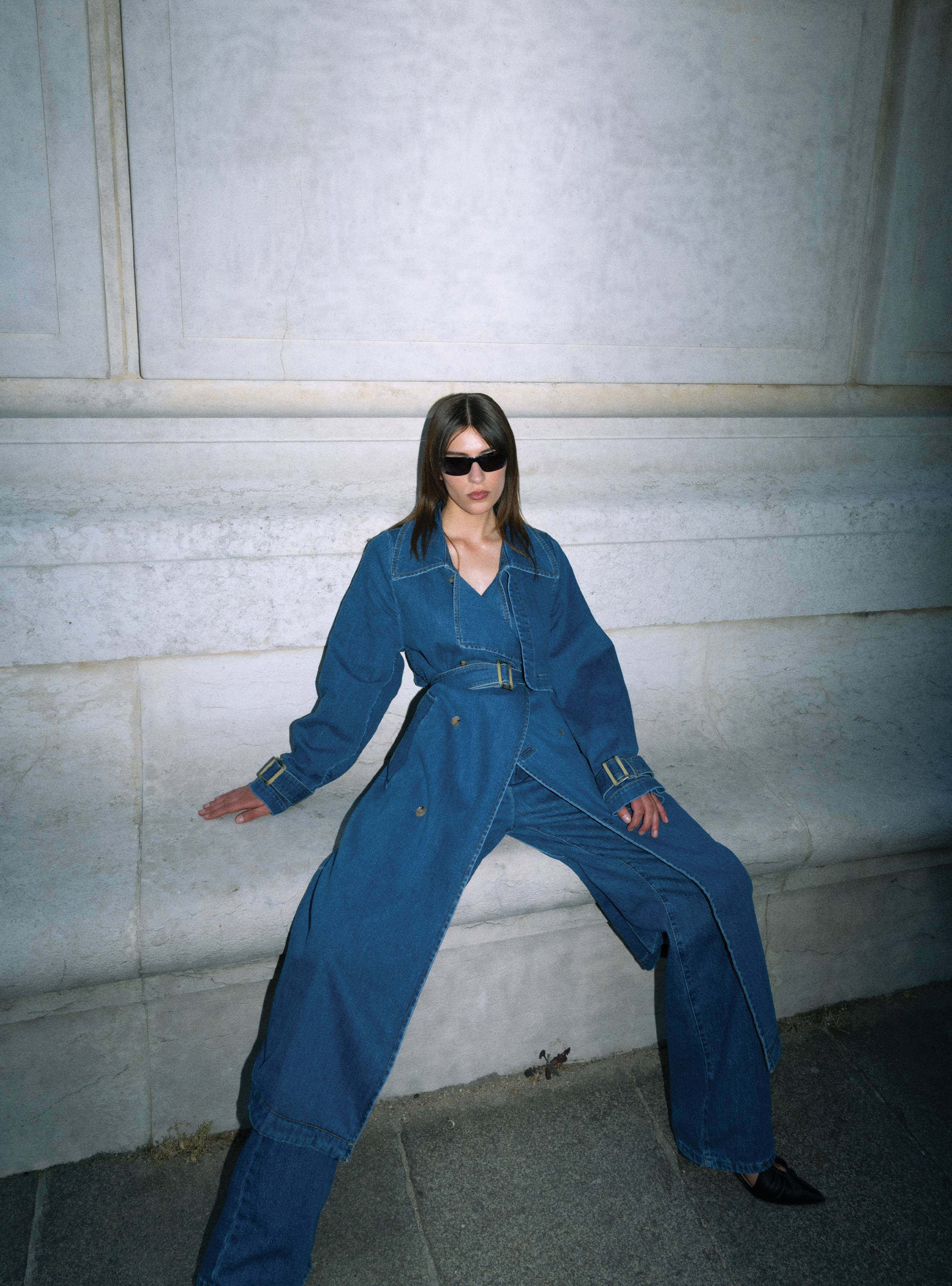 A model sitting wearing the Harriet Denim Blue Denim coat