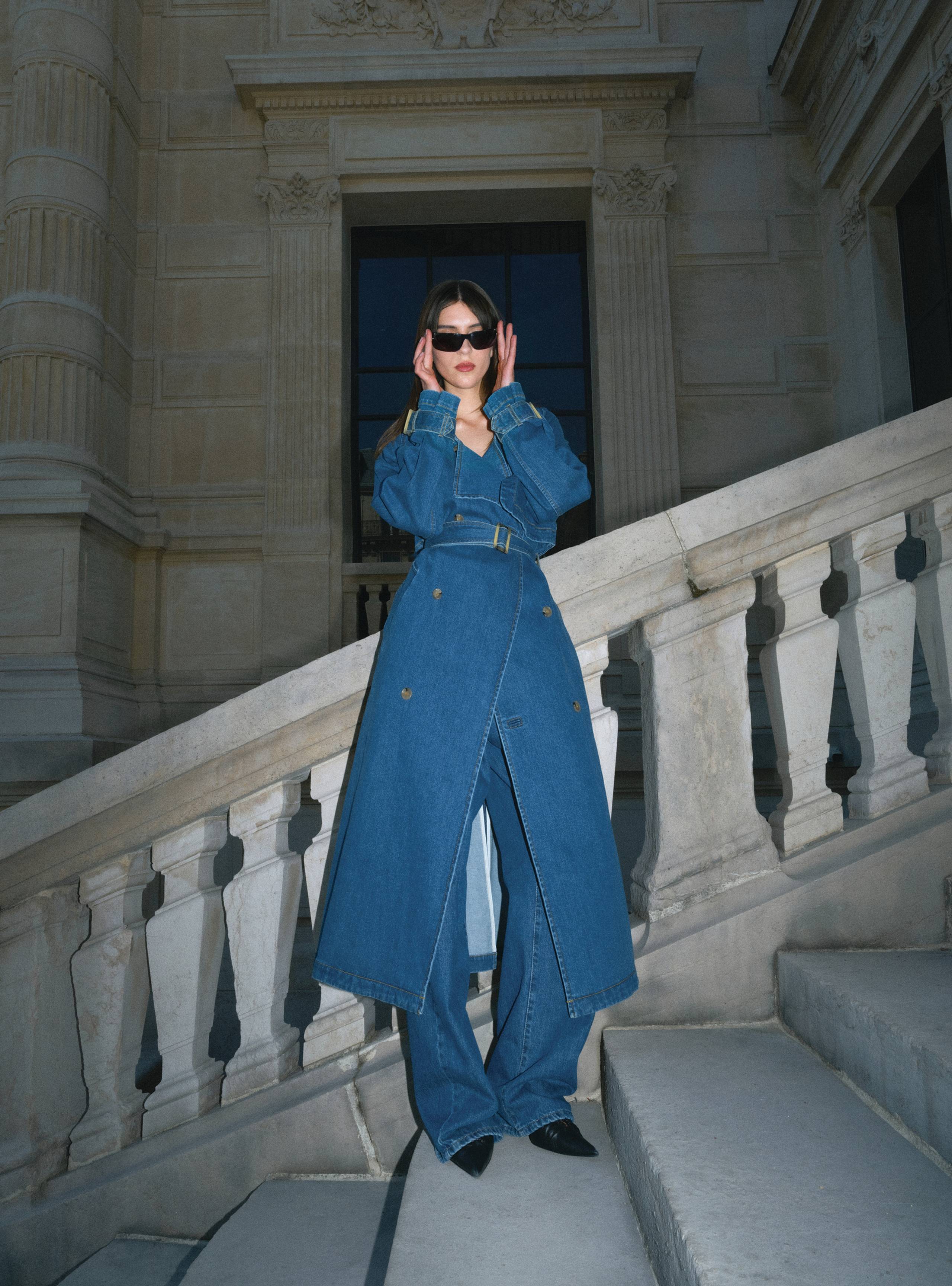 A model standing on a staircase wearing the Harriet Denim Blue Denim coat