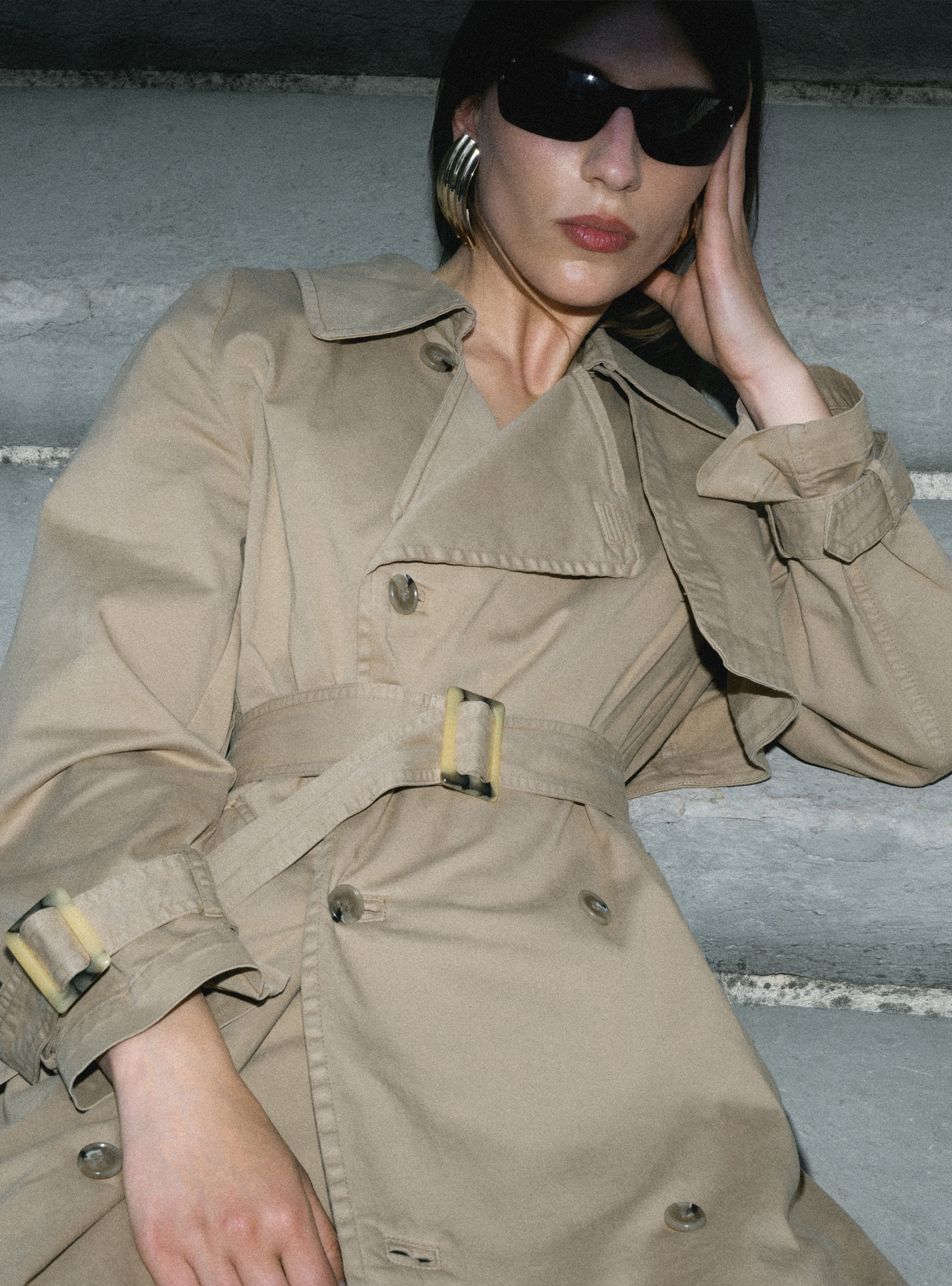 A model sitting on a staircase wearing the Harriet Canvas Khaki trench coat