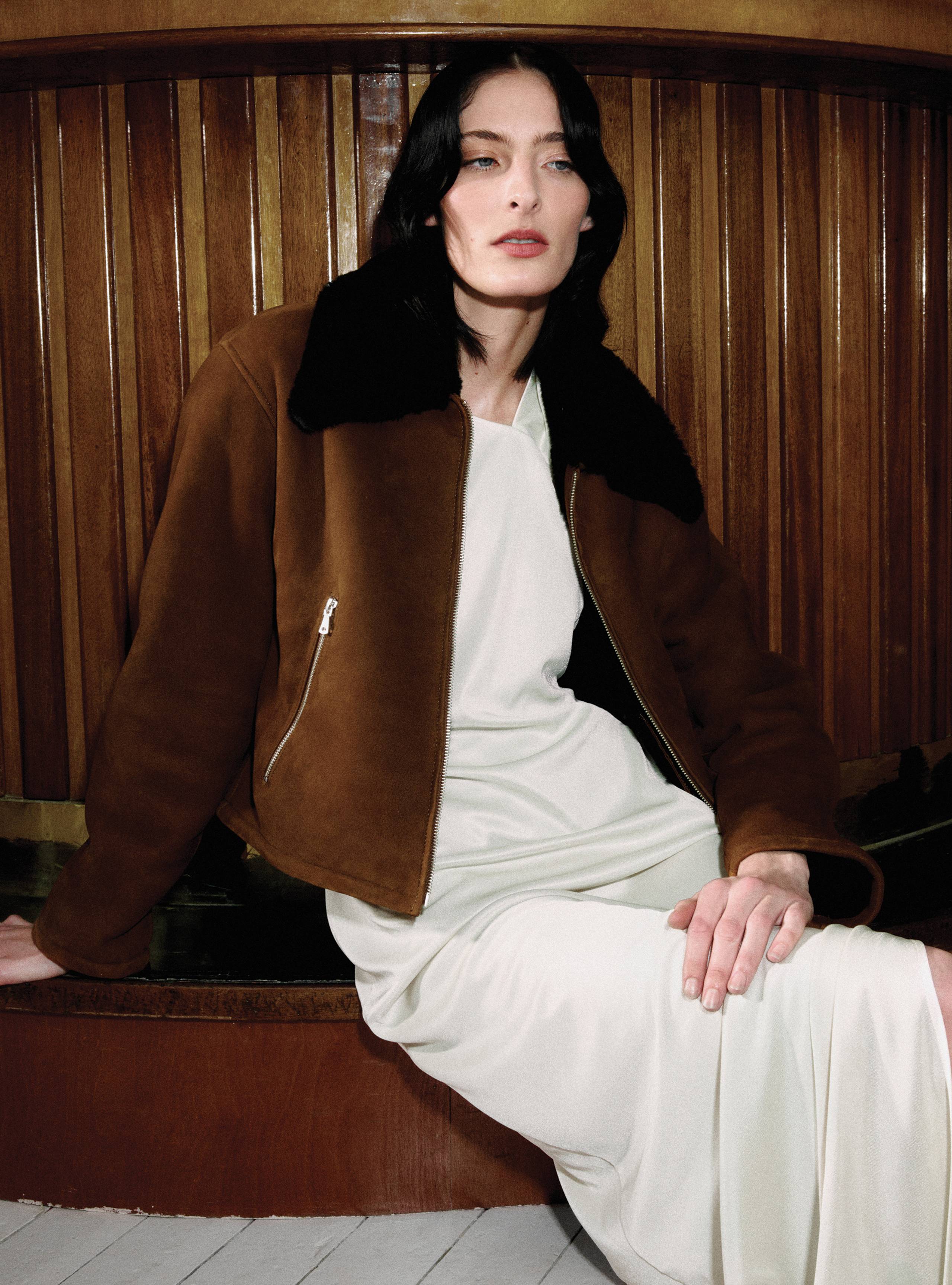 A model sitting on a bench wearing the Nyla Cognac Black jacket