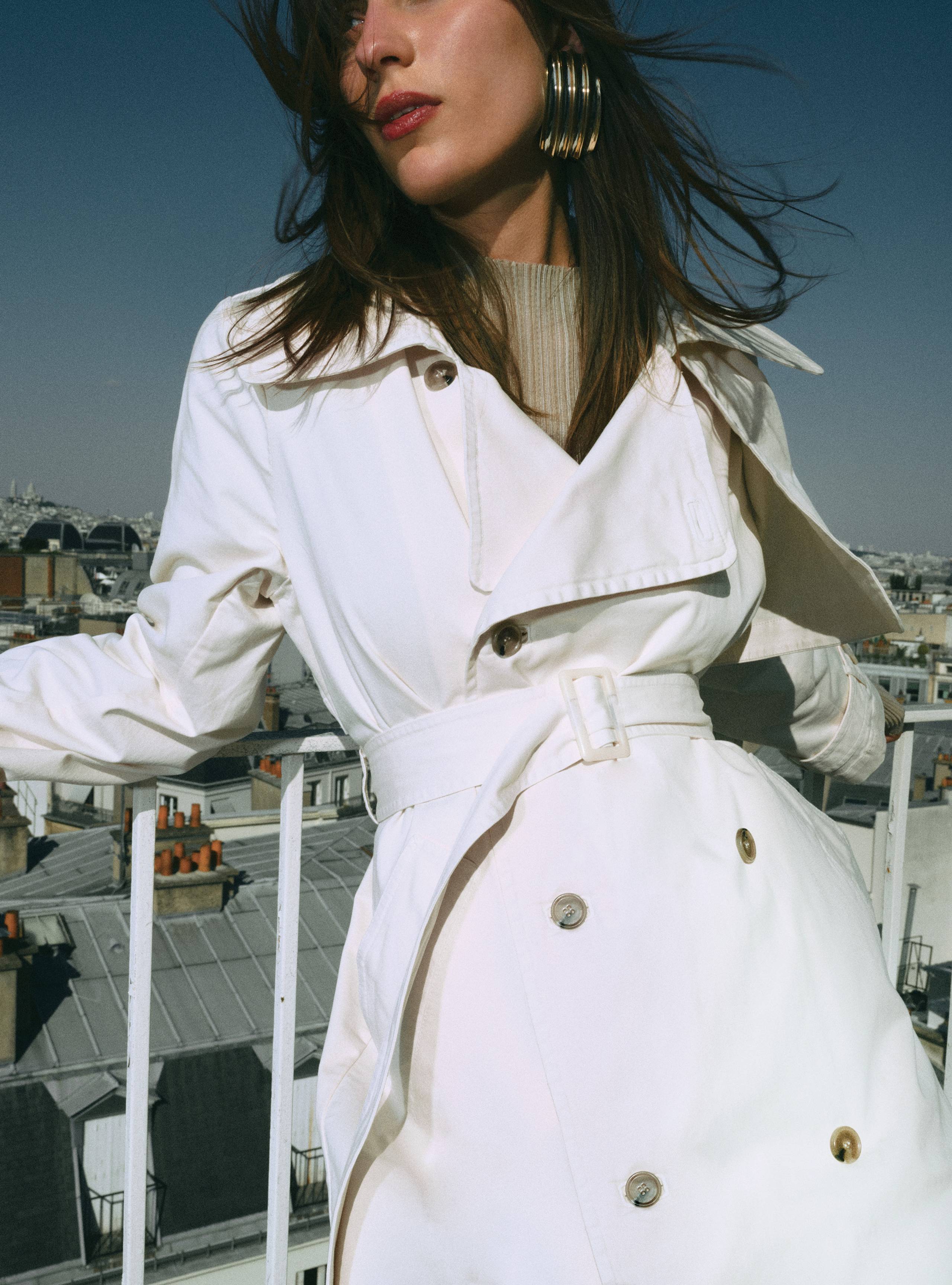 A model leaning on a balcony wearing the Harriet Canvas Cream coat