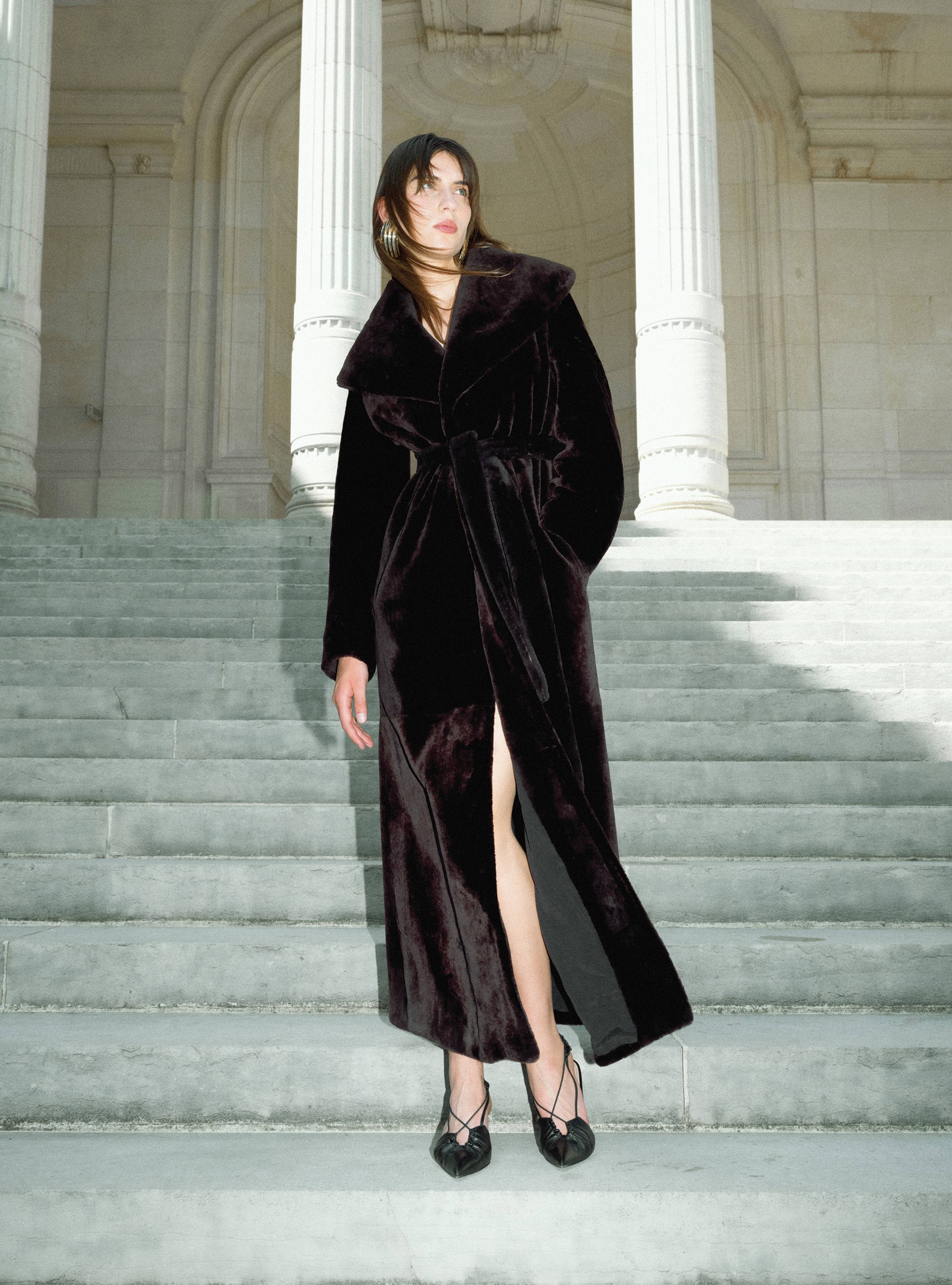 A model standing on a staircase wearing the Giovana Chocolate Fondant long shearling coat
