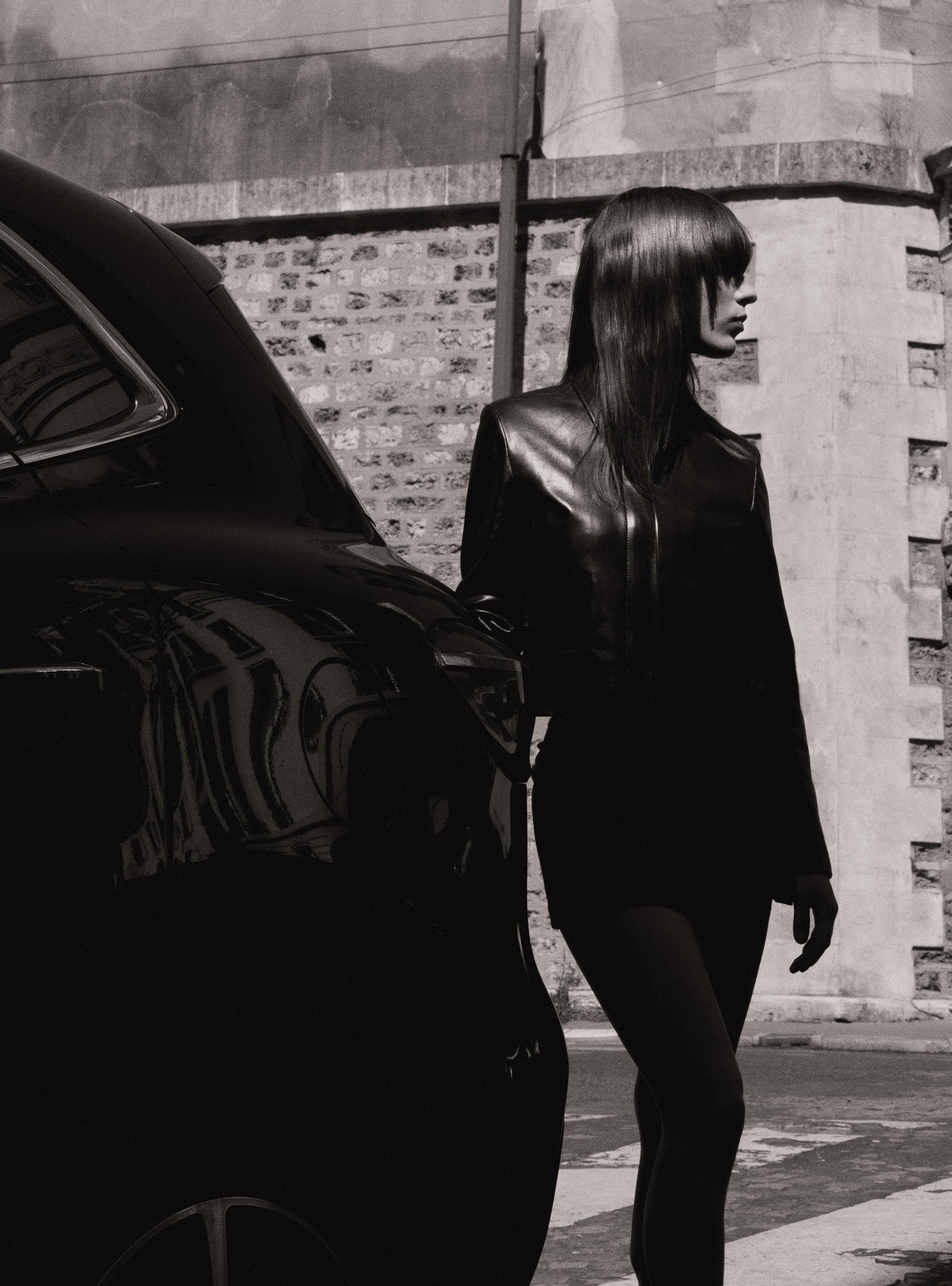 A model standing next to a car wearing the Bleeker Black jacket