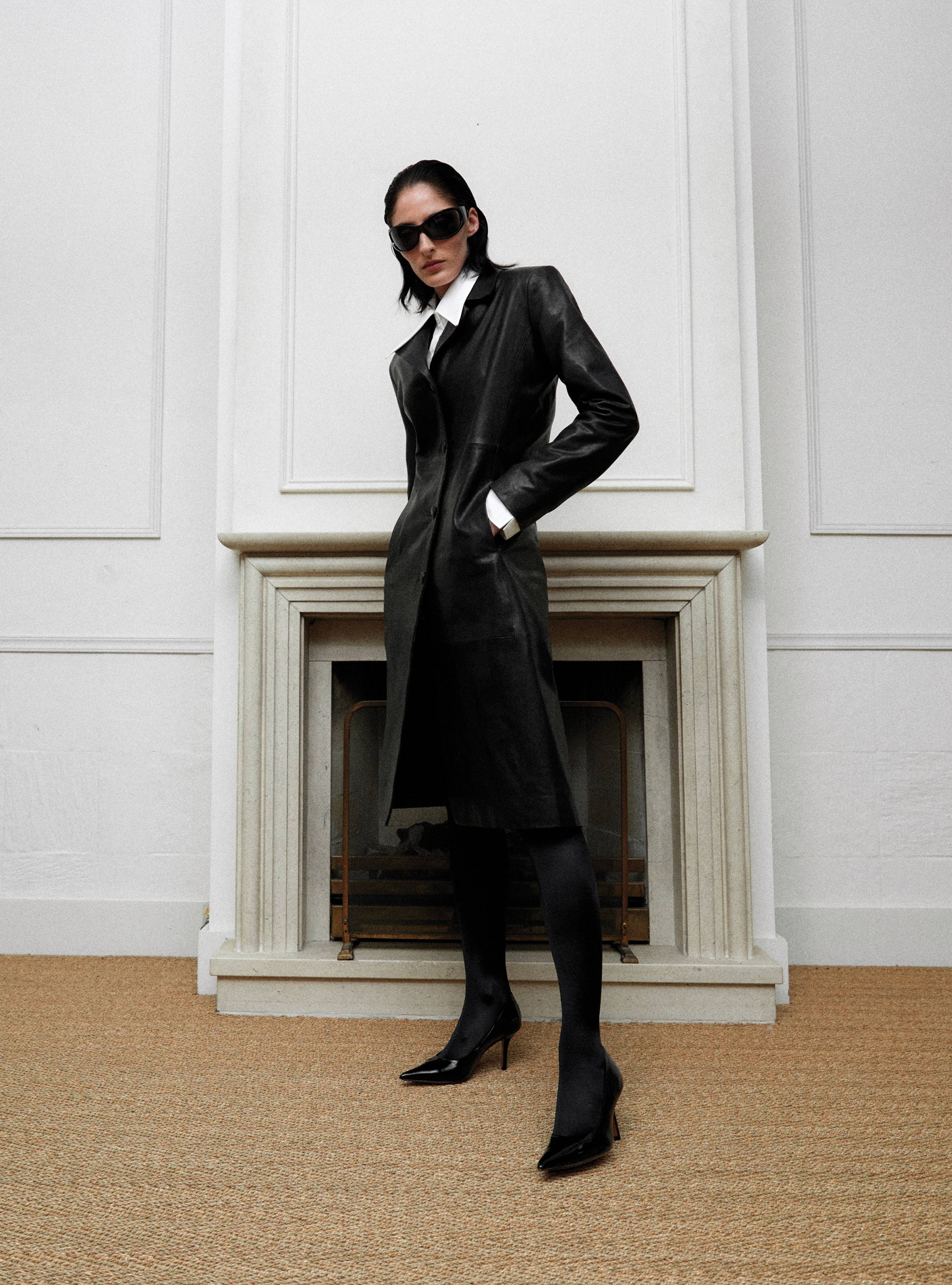 A model standing sideways wearing the Midnight Black long leather coat
