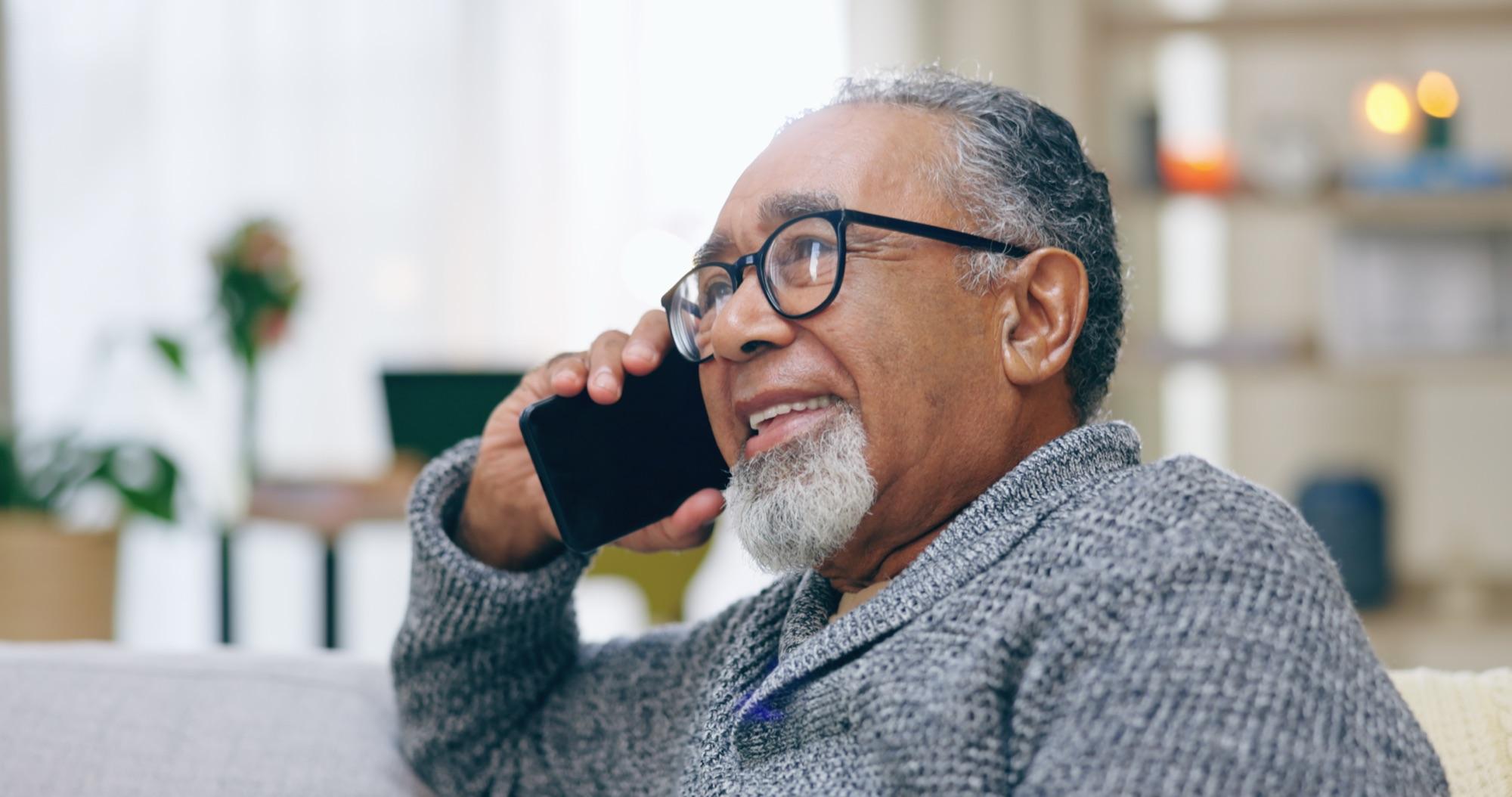 Mann i sekstiårene sitter i sofaen hjemme og snakker i mobiltelefonen