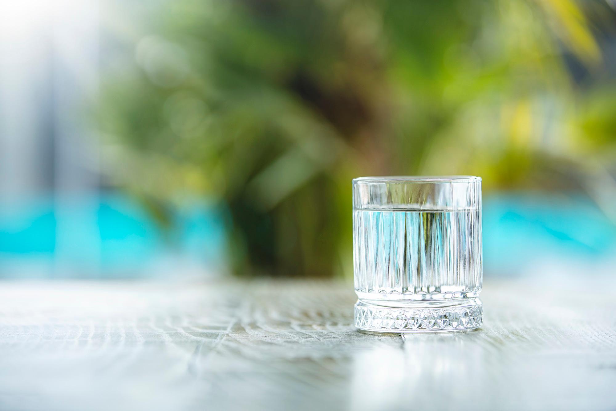 Glass med vann på et bord, med uskarpt grønt utenfor i bakgrunnen