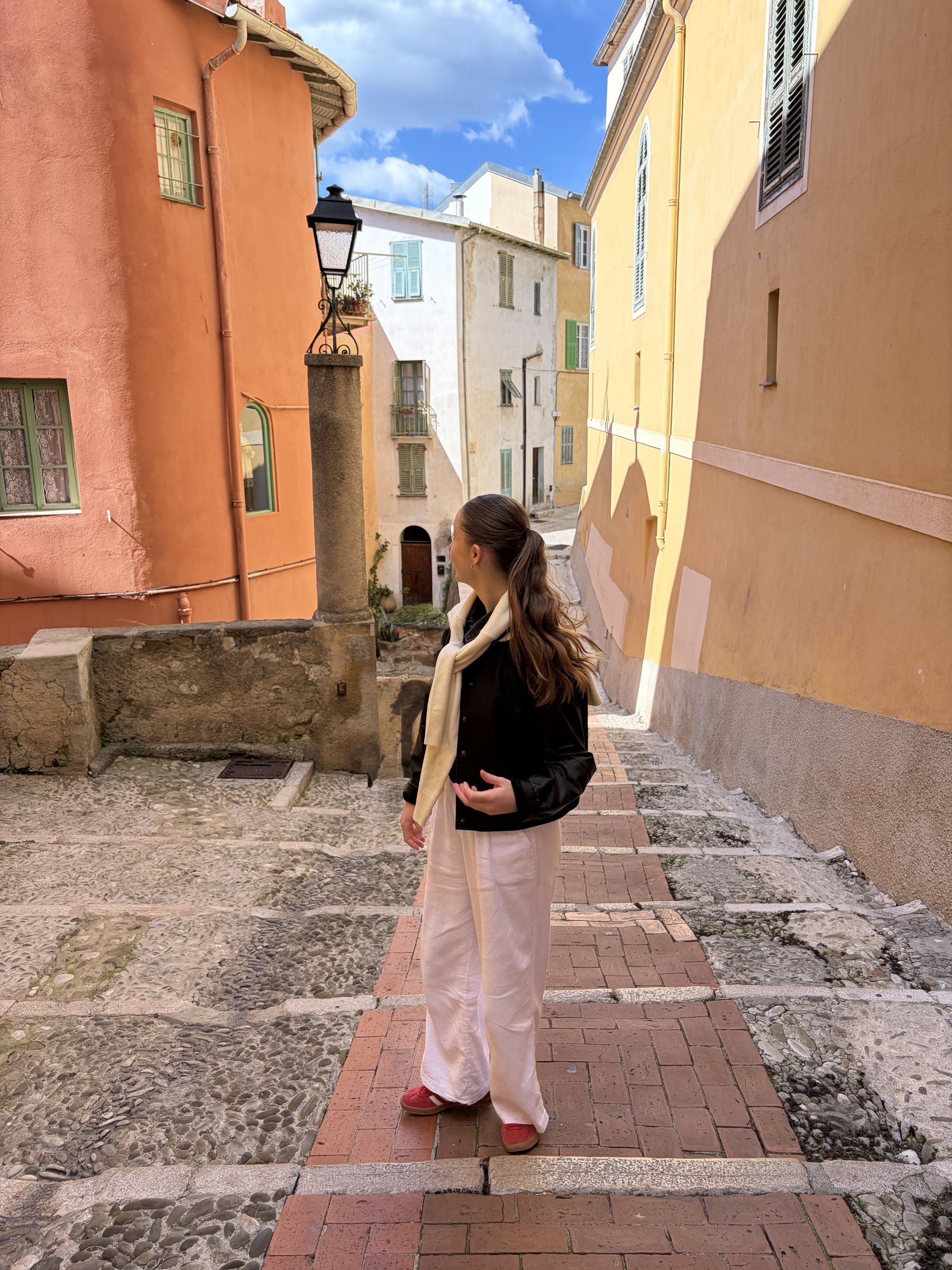 Woman in white linen trousers and red shoes, in Italy-Menton looking at the colorful buildings.