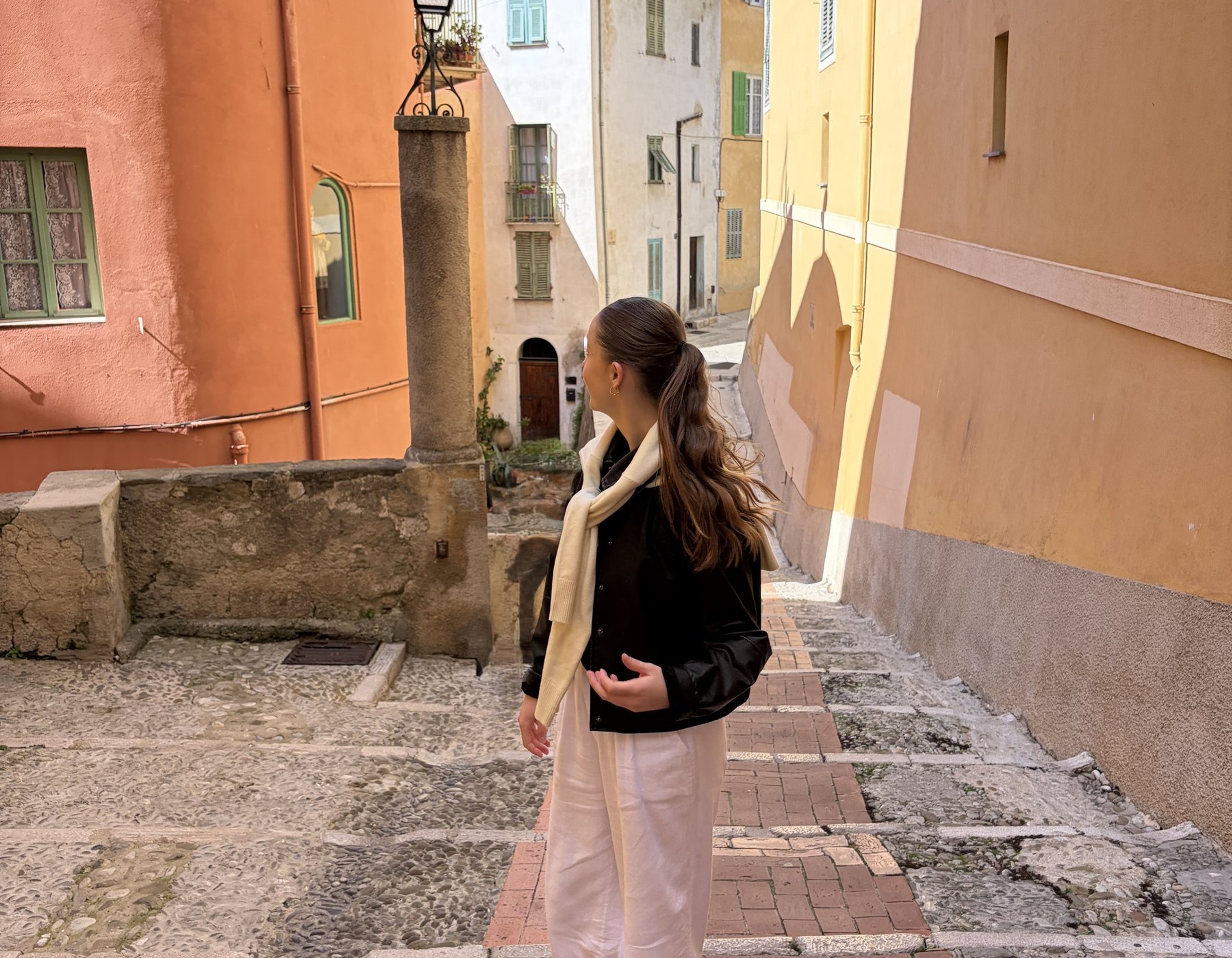 Woman in white linen trousers and red shoes, in Italy-Menton looking at the colorful buildings.