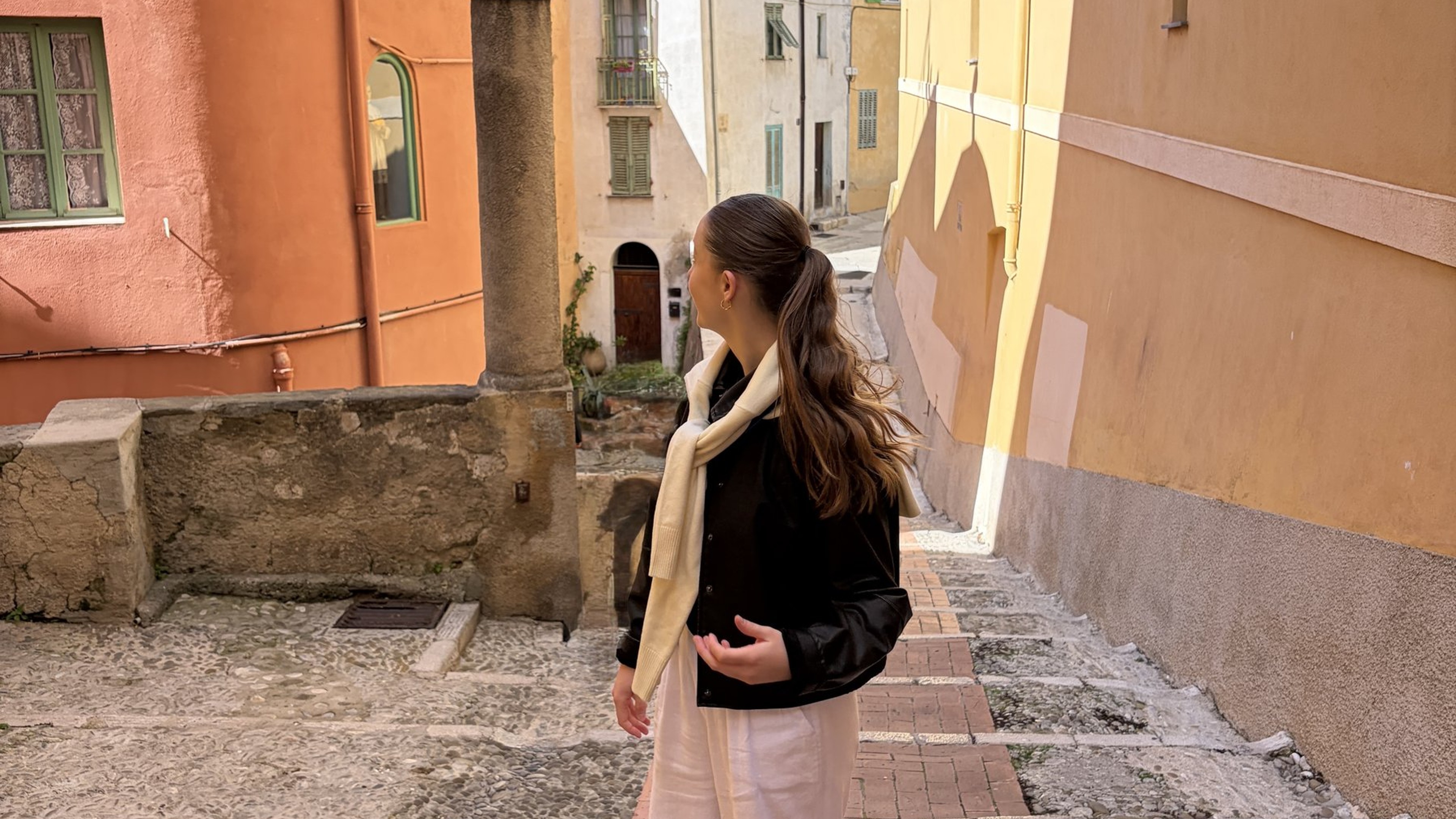Woman in white linen trousers and red shoes, in Italy-Menton looking at the colorful buildings.