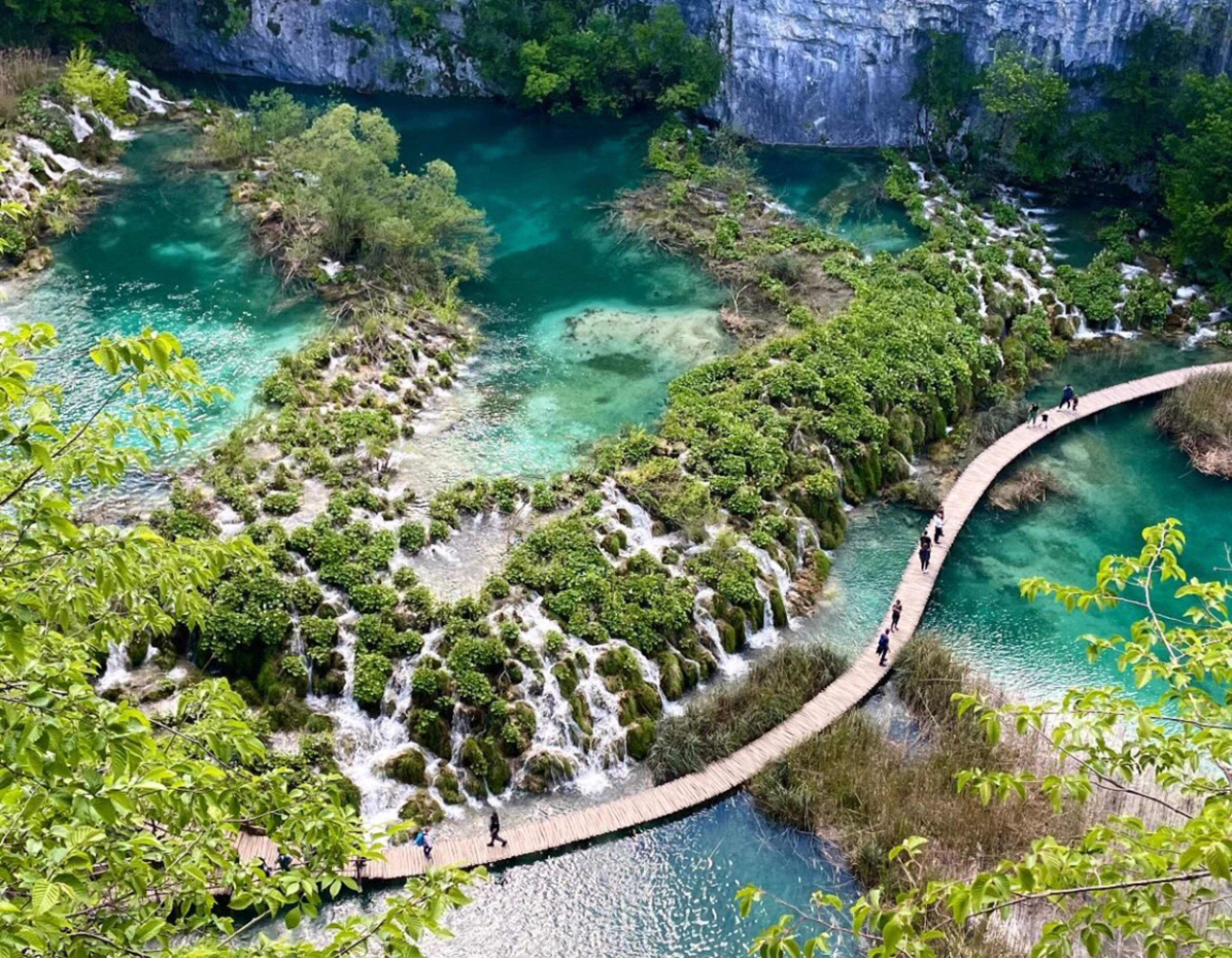 A picture of plitvice lakes national park in Croatia showing a blue/green lake next to a cliff.