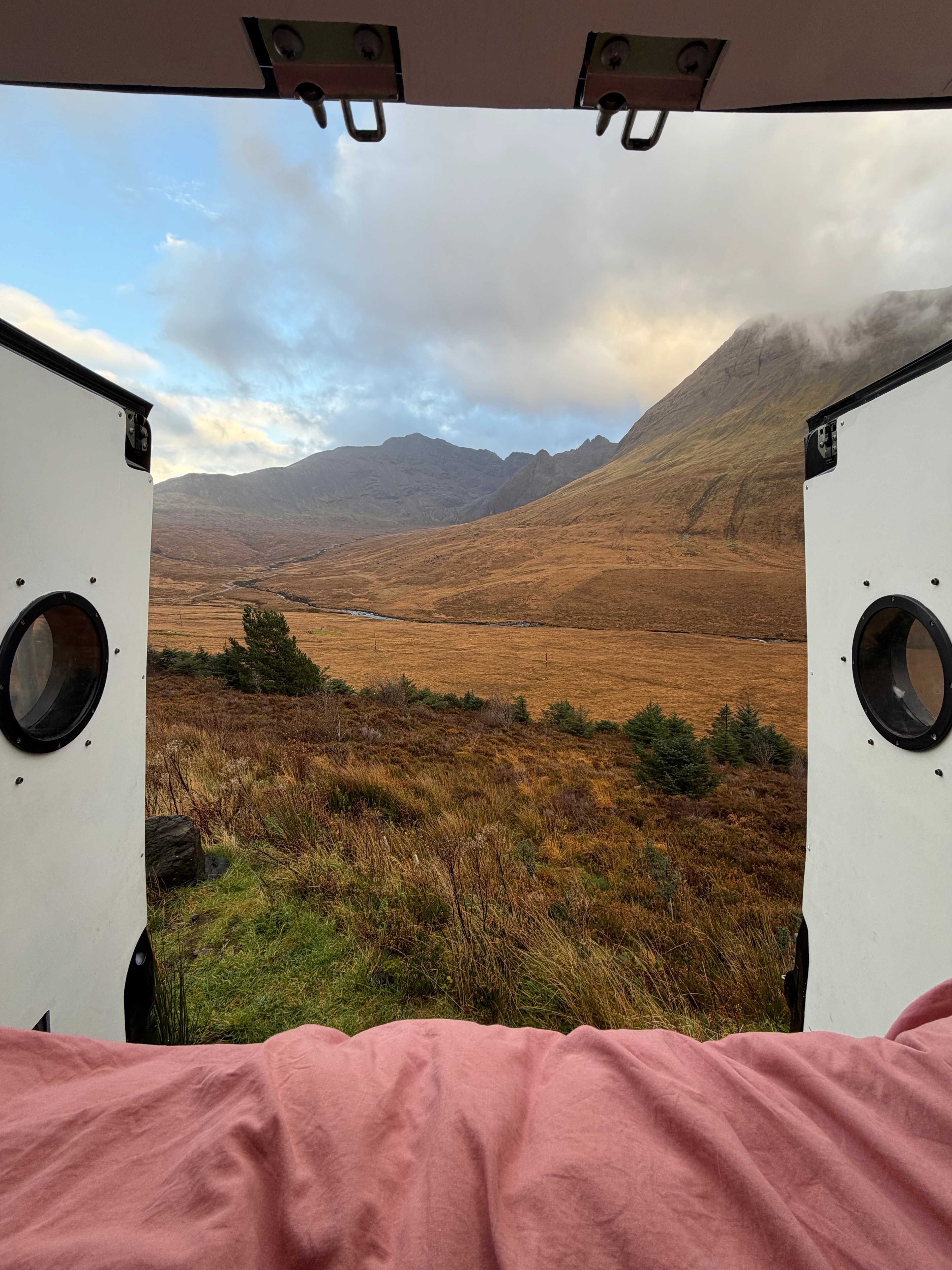Back doors of a converted van open to see the scenery of the mountains in the highlands 