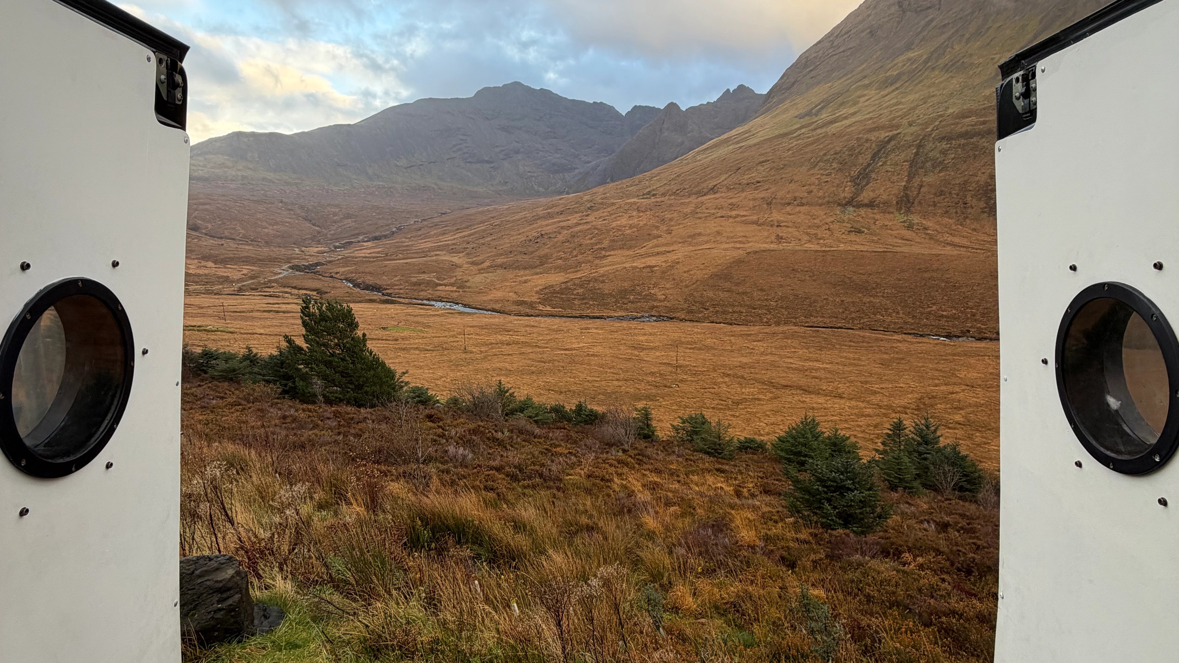 Back doors of a converted van open to see the scenery of the mountains in the highlands