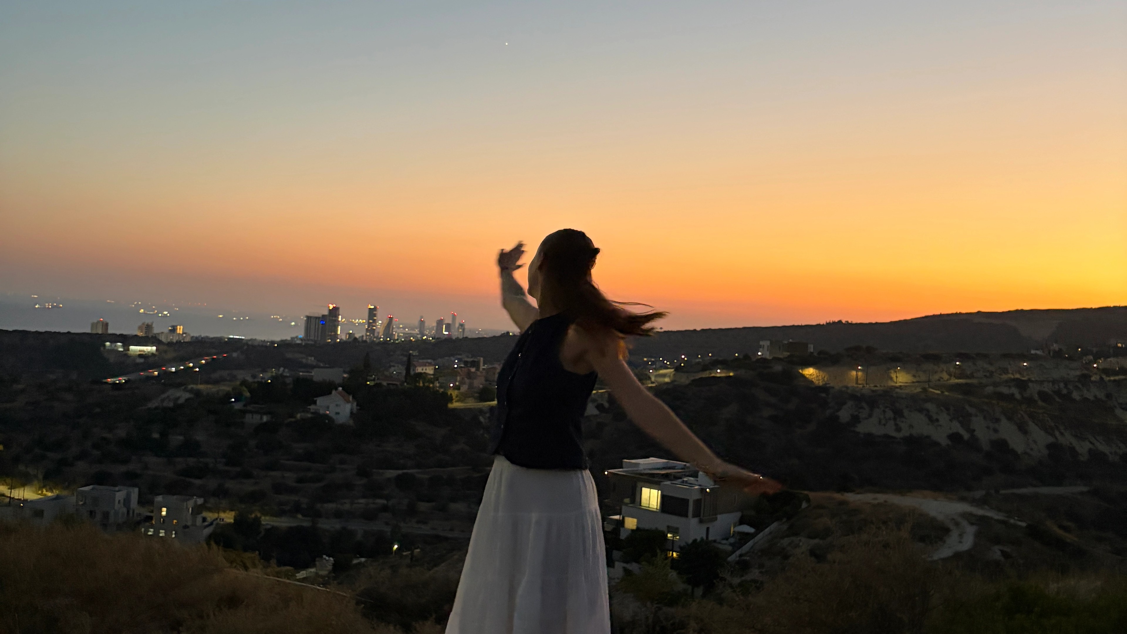 Girl stood on a mountain at sunset looking out at the city horizon