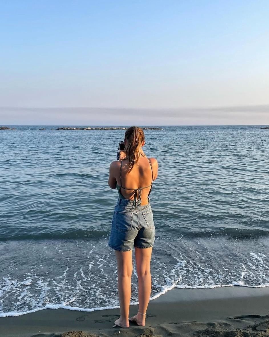 A girl stood on the beach looking out to sea holding a film camera and taking a picture.