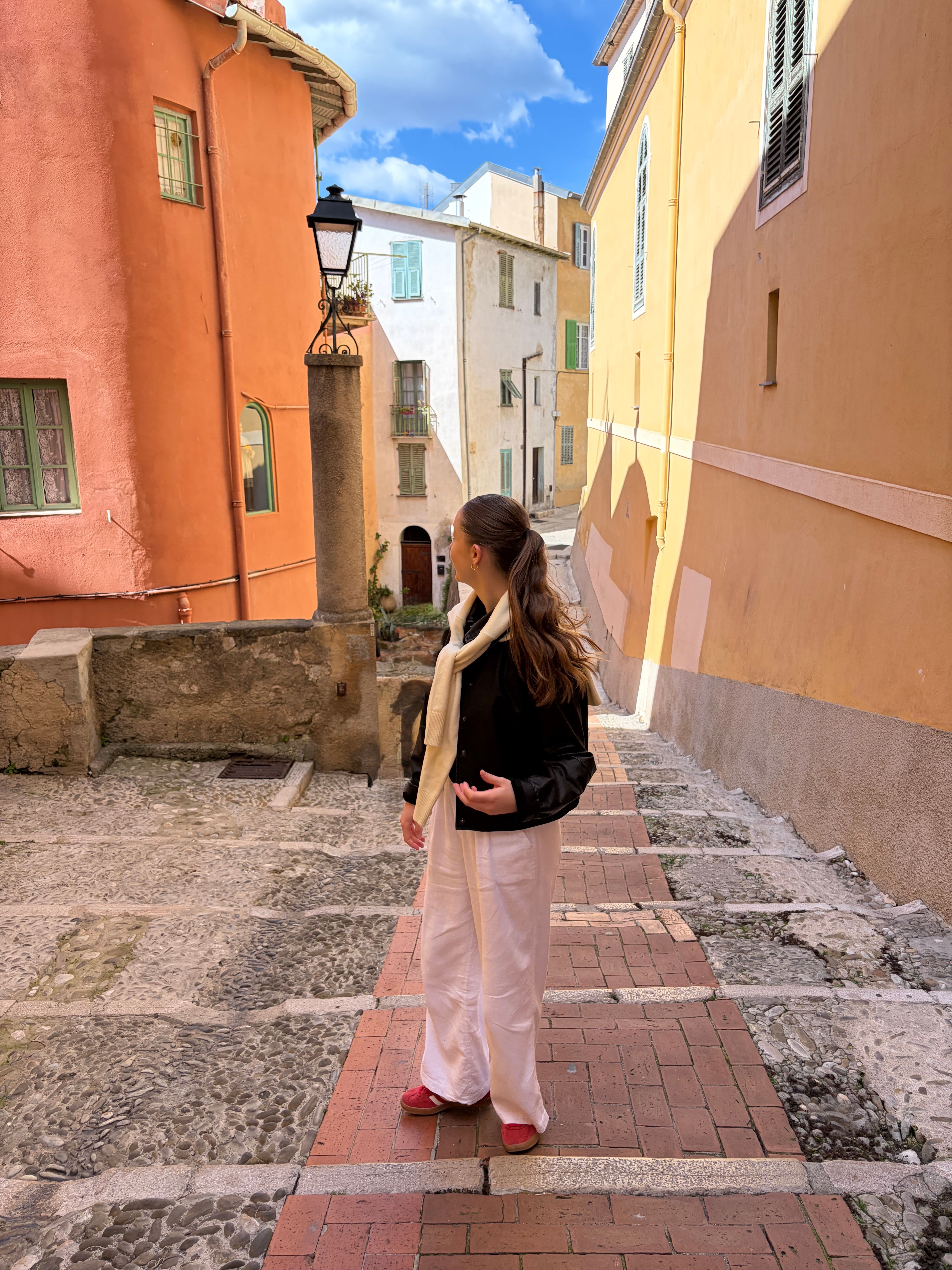 Woman in white linen trousers and red shoes, in France looking at the colourful buildings.