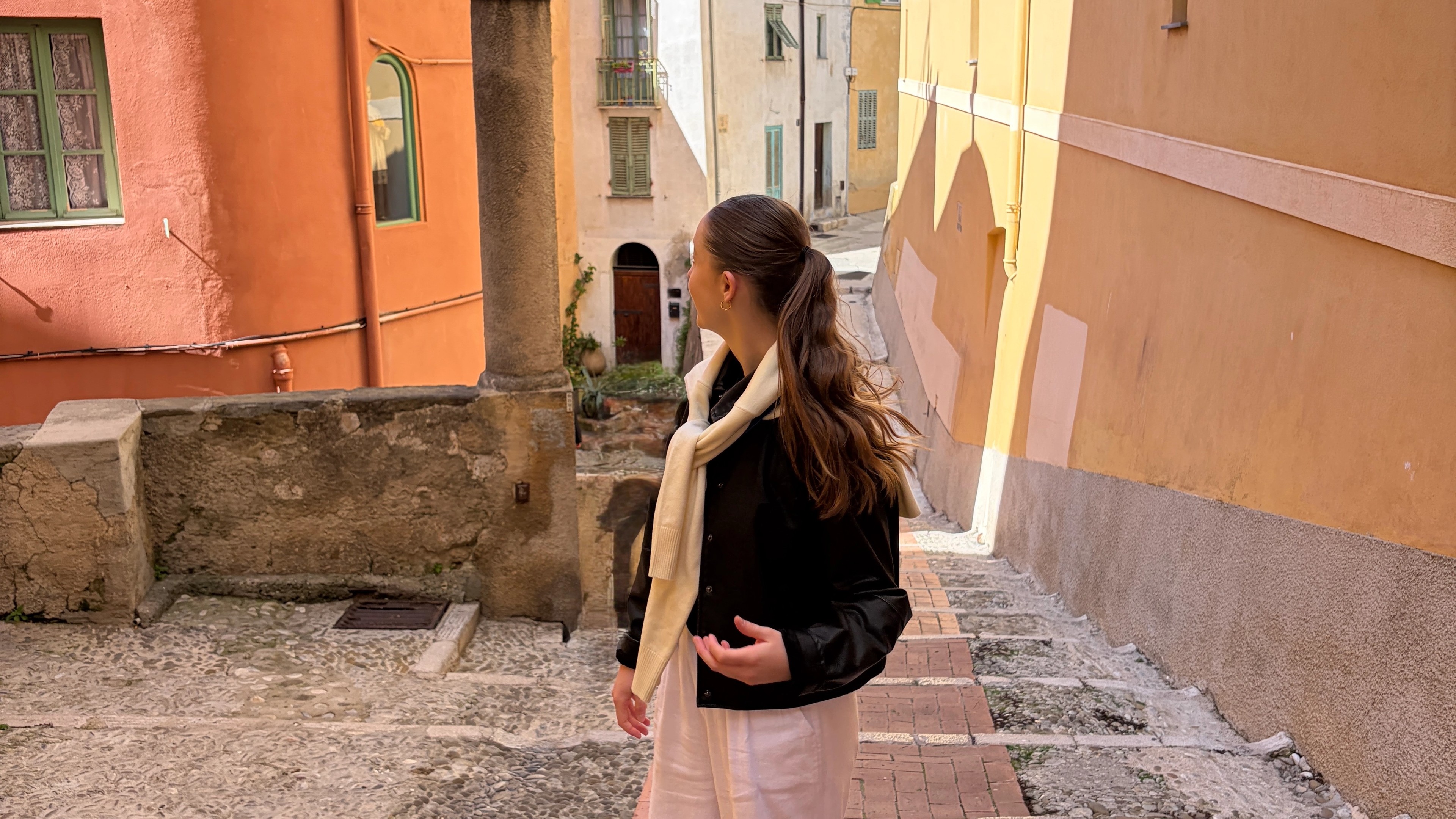 Woman in white linen trousers and red shoes, in France looking at the colourful buildings.