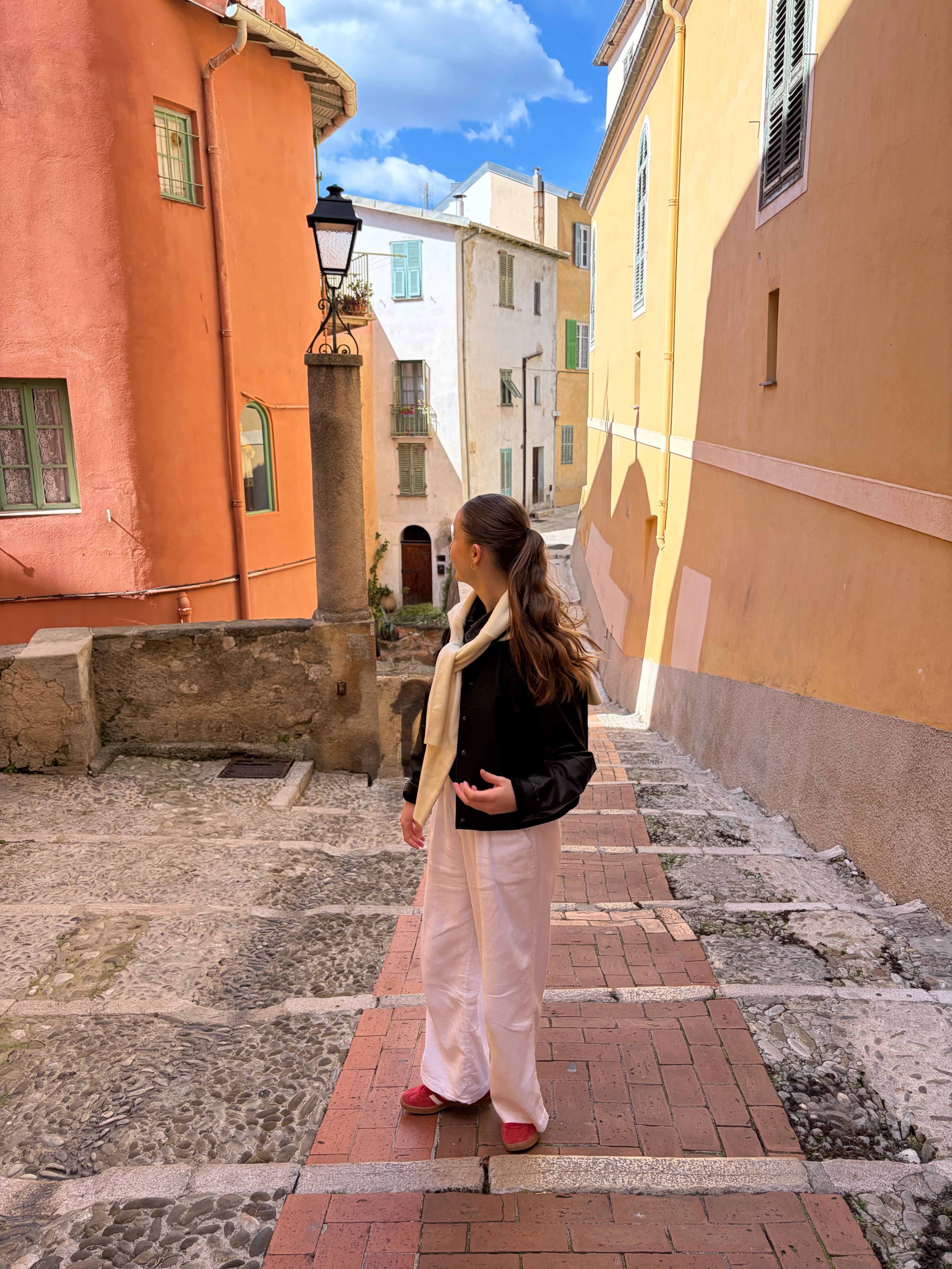 Woman in white linen trousers and red shoes, in France looking at the colourful buildings.