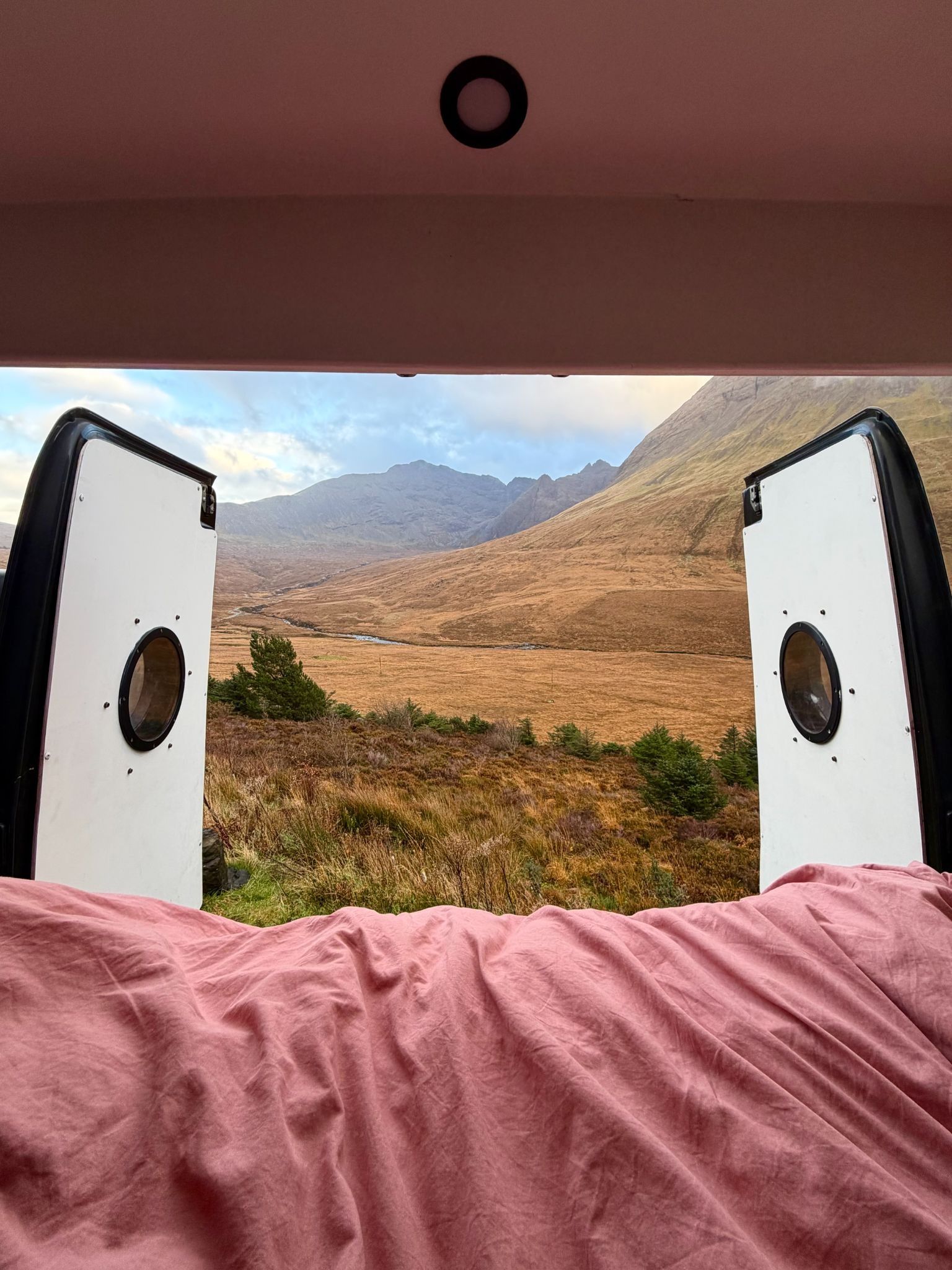 Back doors of a converted van open to see the scenery of the mountains in the highlands 