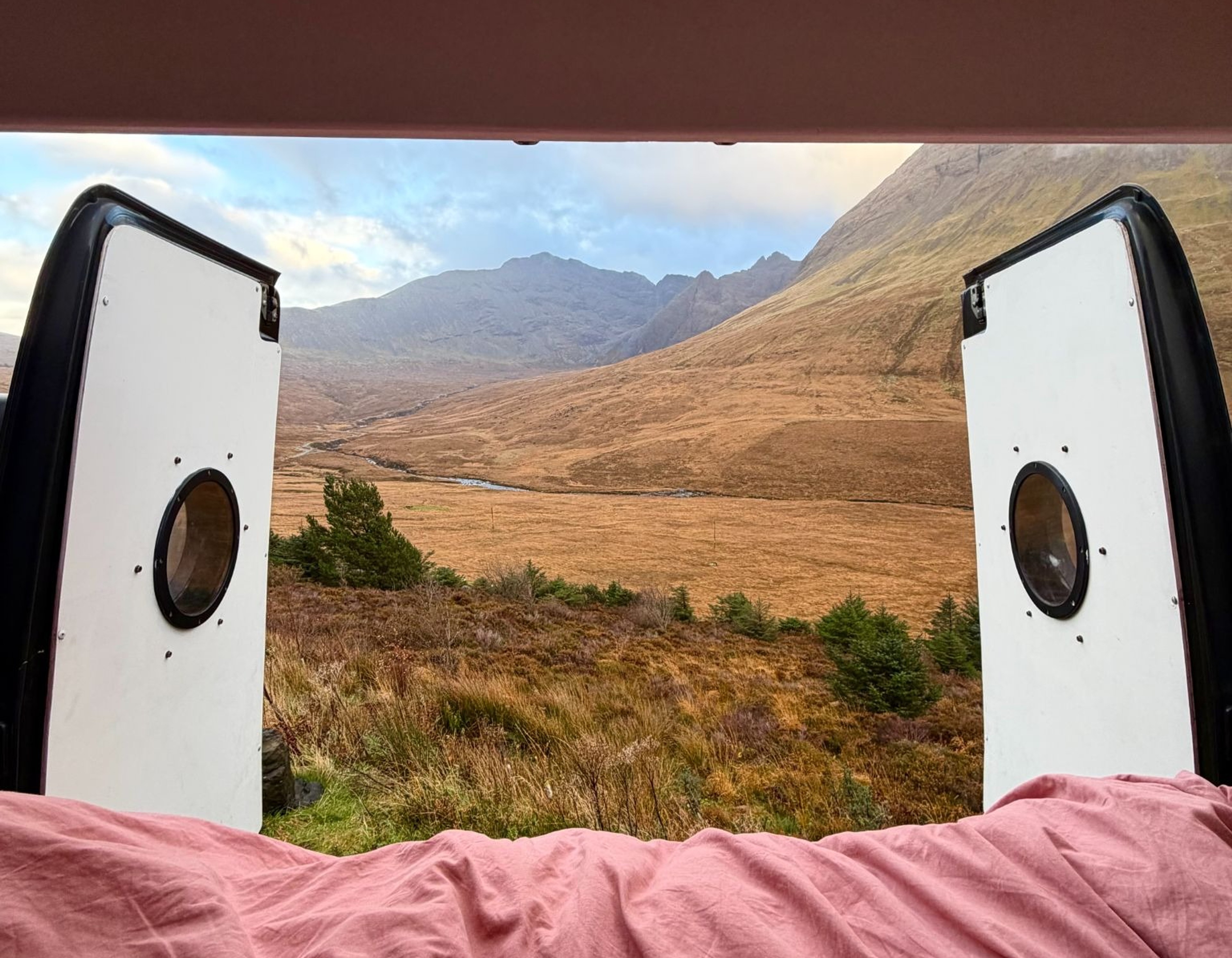 Back doors of a converted van open to see the scenery of the mountains in the highlands