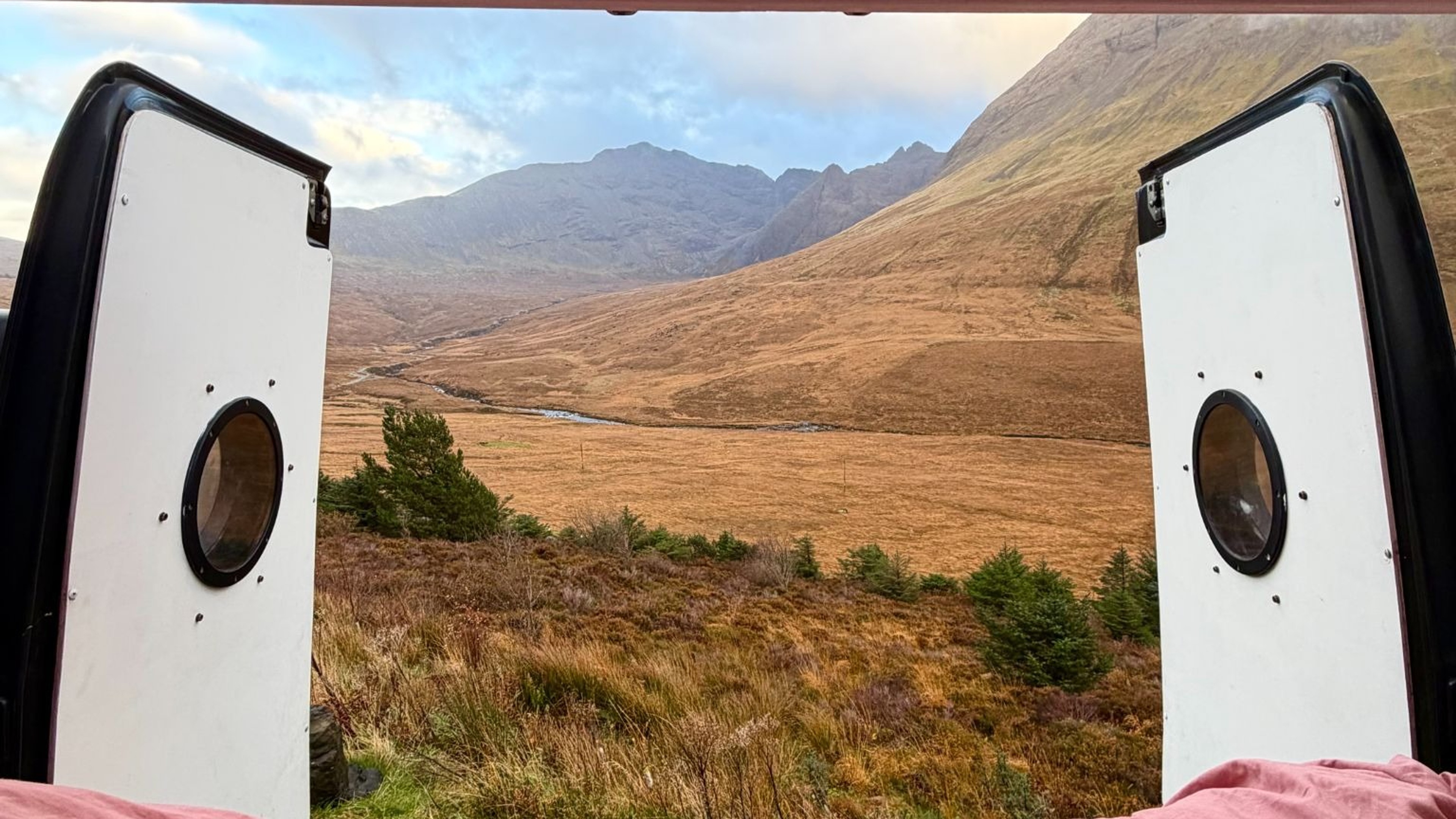 Back doors of a converted van open to see the scenery of the mountains in the highlands