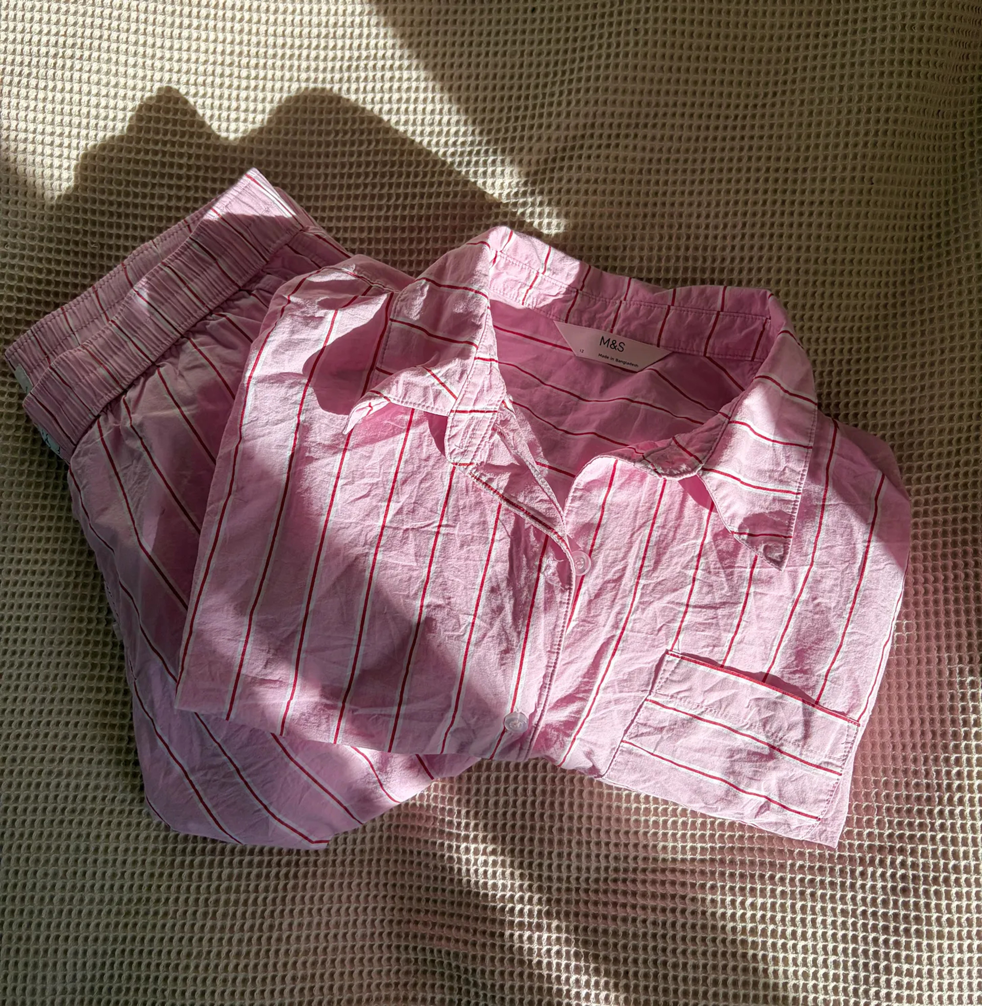 A set of button up striped pick pajamas folded neatly on a beige bed. 