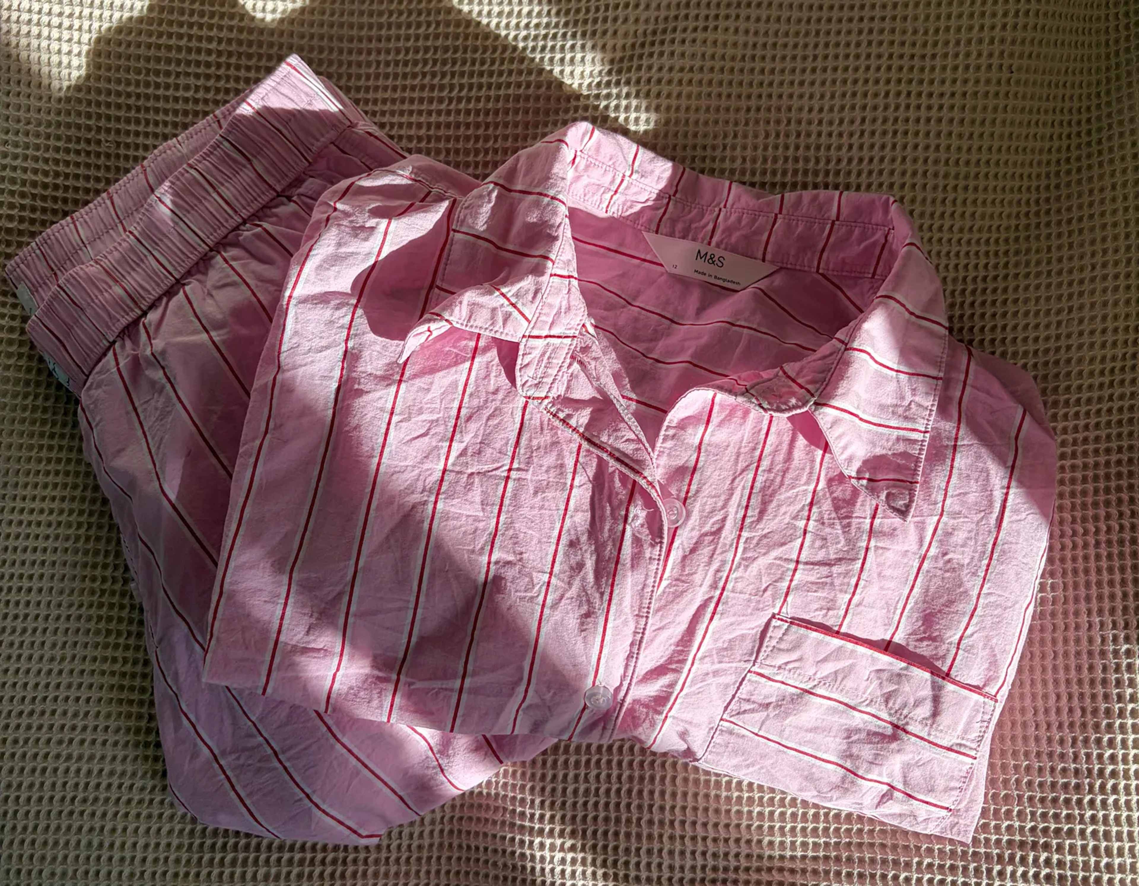 A set of button up striped pick pajamas folded neatly on a beige bed.