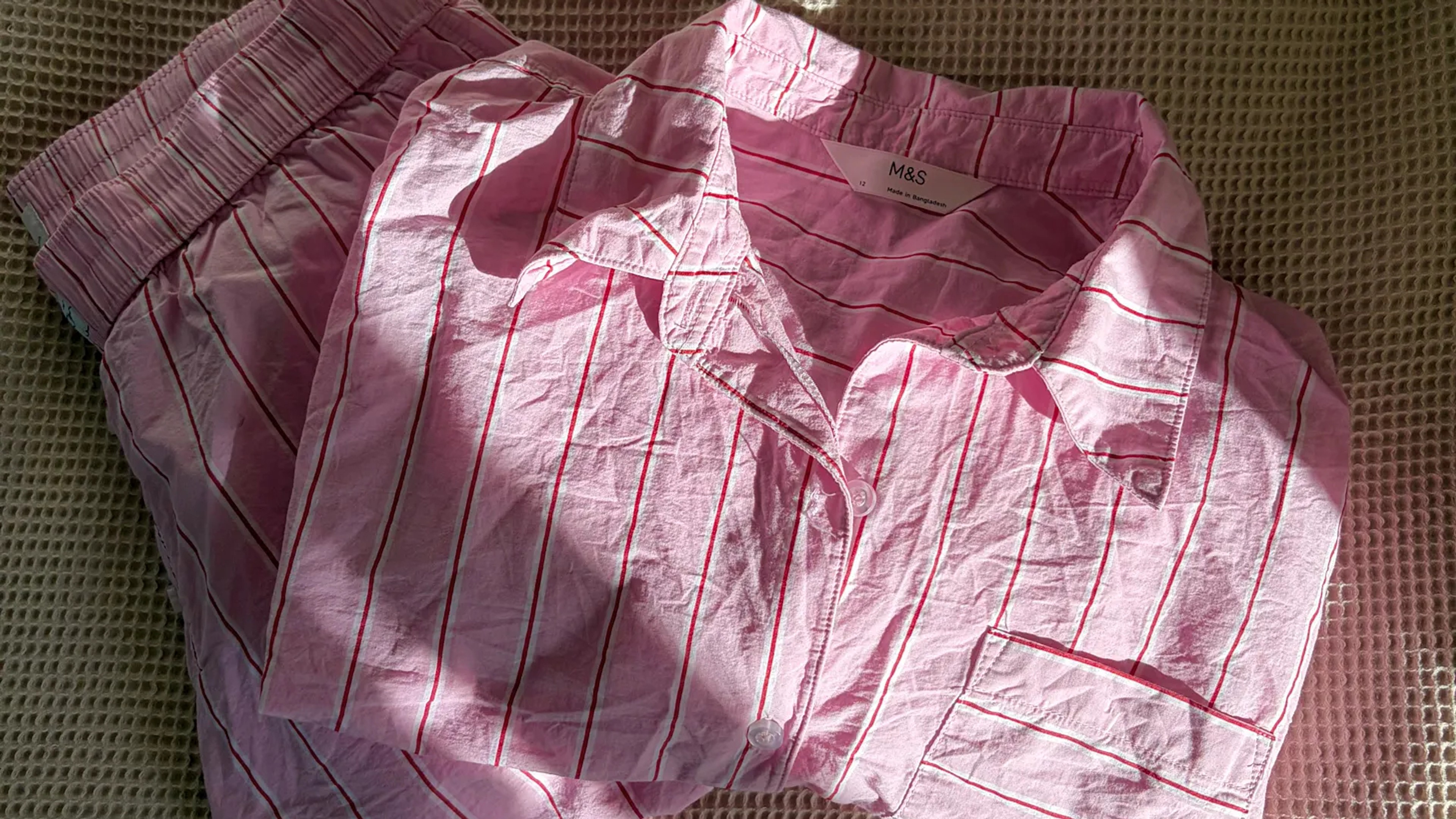 A set of button up striped pick pajamas folded neatly on a beige bed.