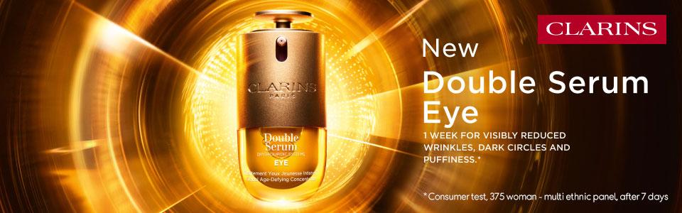 Clarins advertisement for New Double Serum Eye, featuring a golden bottle with text promoting reduced wrinkles, dark circles, and puffiness.