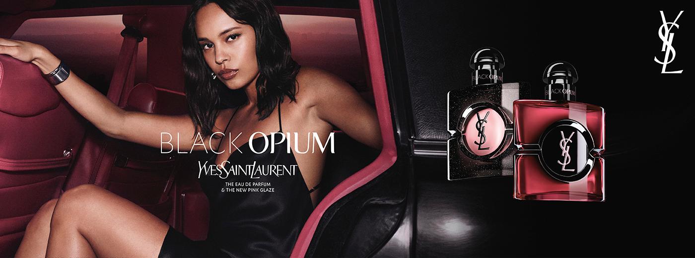 Yves Saint Laurent Black Opium perfume ad featuring a woman in a car with two perfume bottles, one black with pink and one bright pink.