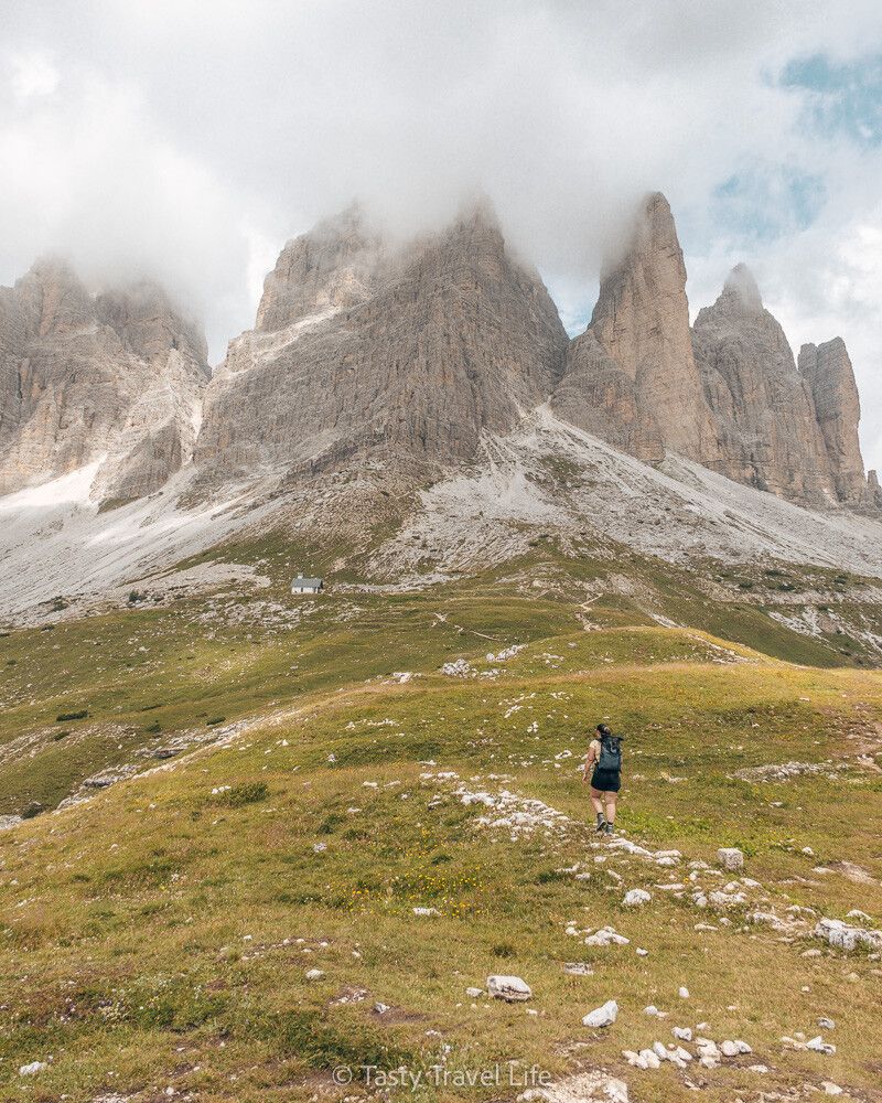 Moi, marchant sur un sentier dans l'herbe vers d'immenses sommets montagneux. Nuages au-dessus des sommets.