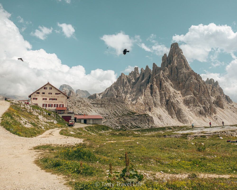 Vue du refuge Dreizinnen et des montagnes en arrière-plan. Deux oiseaux traversent l'image.