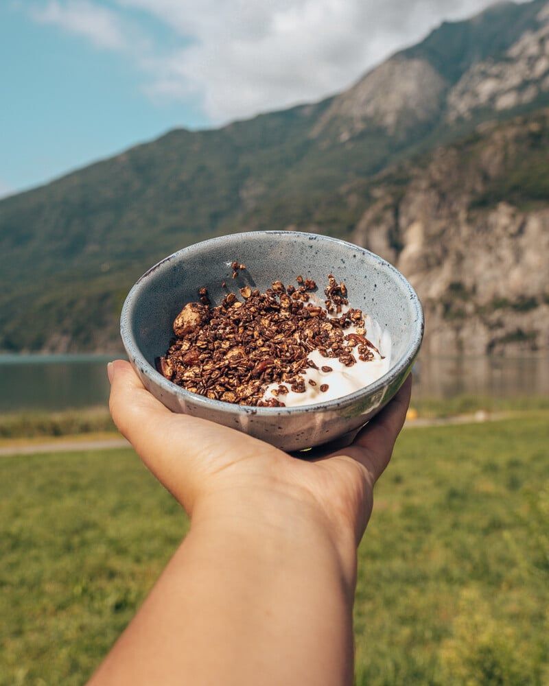 Muesli croustillant au chocolat avec du yaourt dans un bol devant une montagne et un lac.