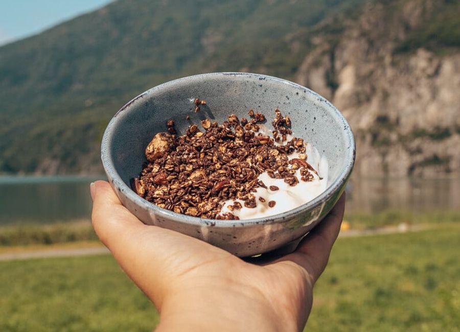Krokante chocolademuesli met yoghurt in een kom voor een berg en meer.