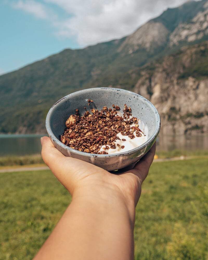 Knapperige chocolademuesli met yoghurt in een kom voor een berg en meer.