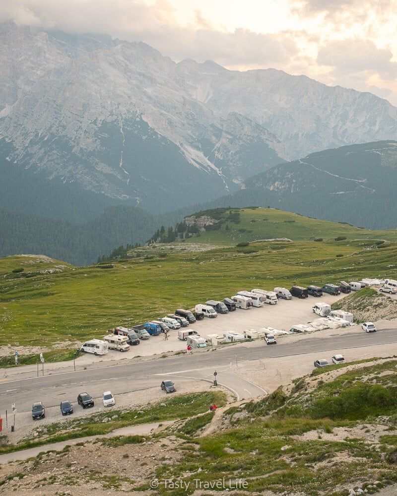 Vue plongeante sur le parking de nuit pour camping-cars du Rifugio Auronzo, avec la vallée et les montagnes en arrière-plan.