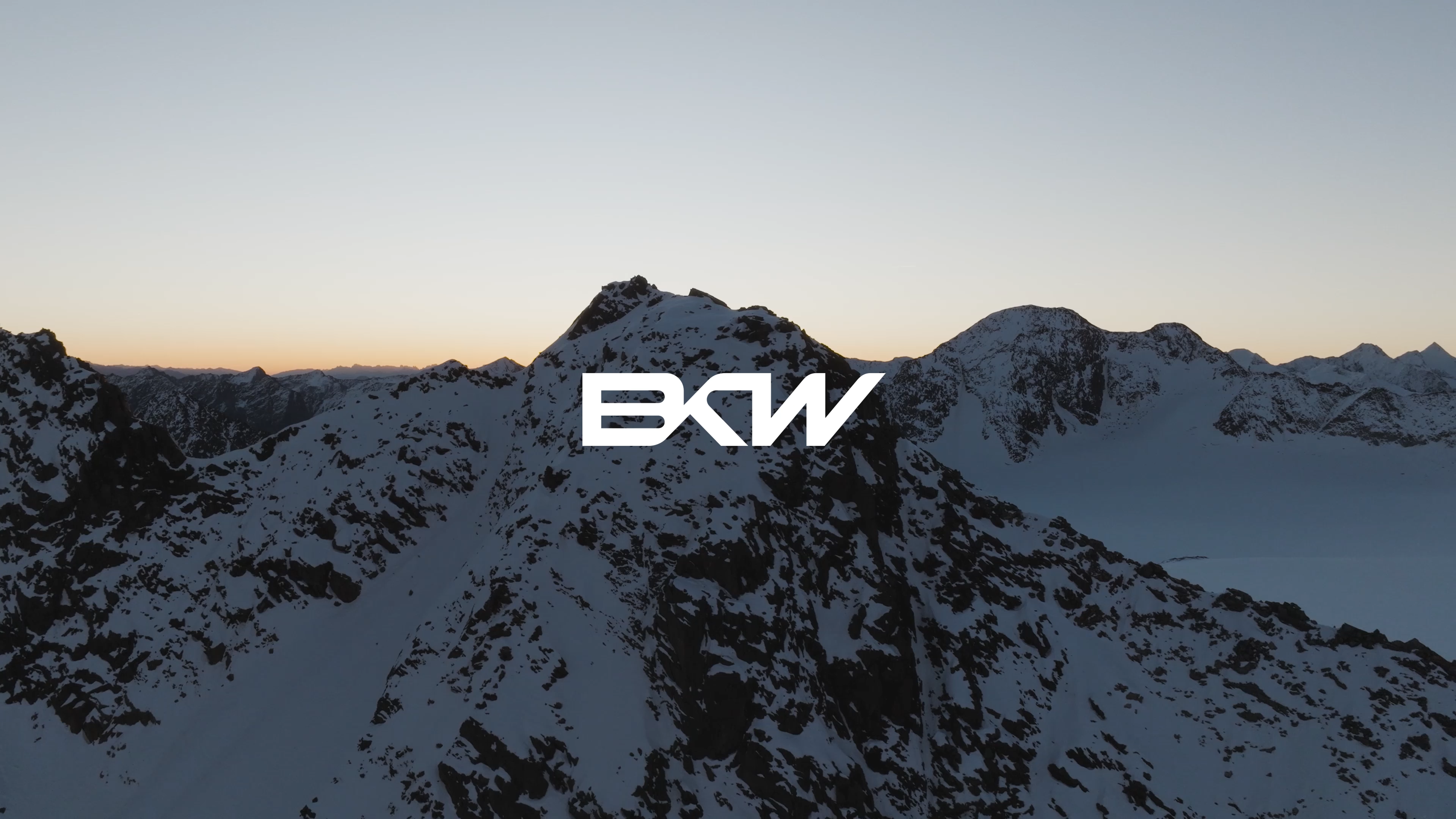 BKW Logo vor schneebedeckten Alpen, Skifahrer und Bergstation