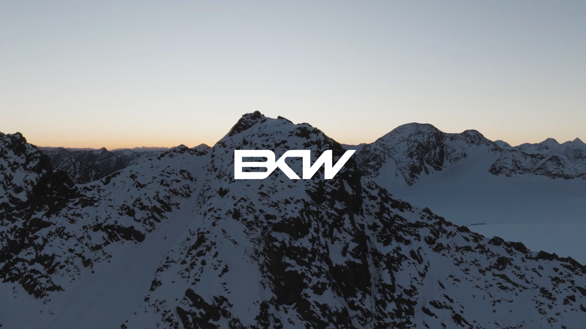 BKW Logo vor schneebedeckten Alpen, Skifahrer und Bergstation