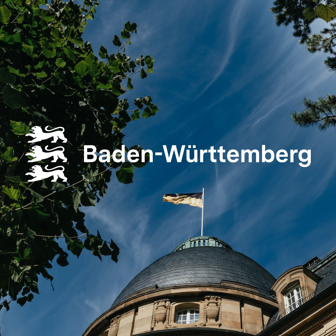 Logo von Baden-Württemberg vor Staatskanzlei mit wehender Flagge